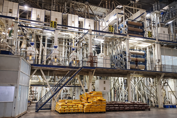 Industrial food processing plant with machinery and stacks of bagged food products on the floor.