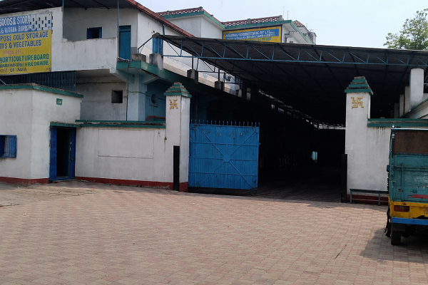 A building with blue gates, partially covered parking area, and signs with yellow and blue text in an urban setting.