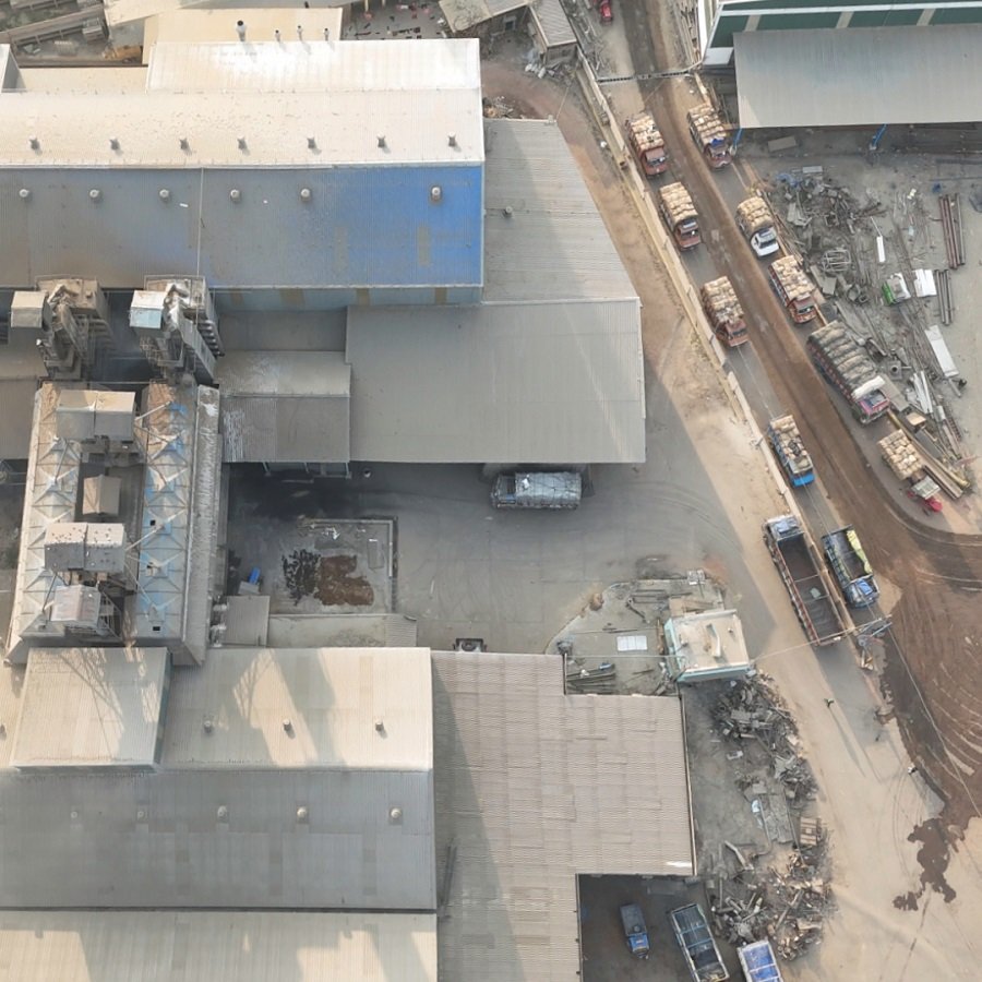 Aerial view of a construction site with multiple industrial buildings, parked vehicles, and construction materials on dirt roads.