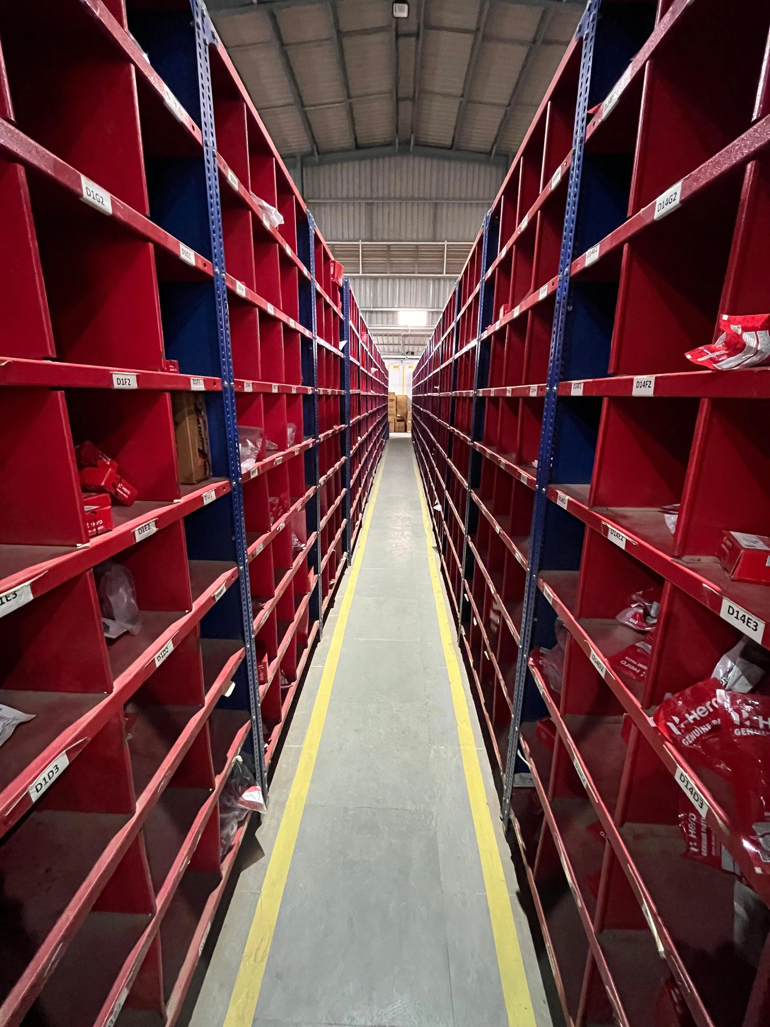 Empty metal shelves with red bins in a warehouse aisle.