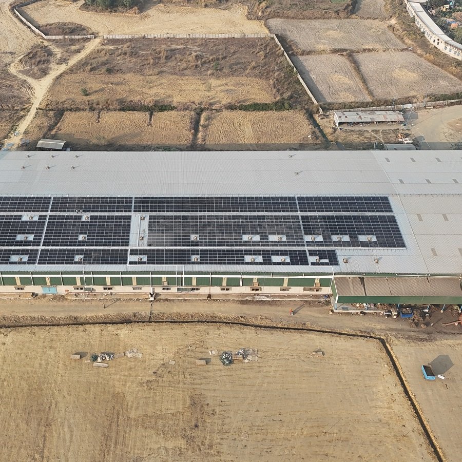 Aerial view of a building with solar panels on the roof, surrounded by open land with fields and dirt paths.