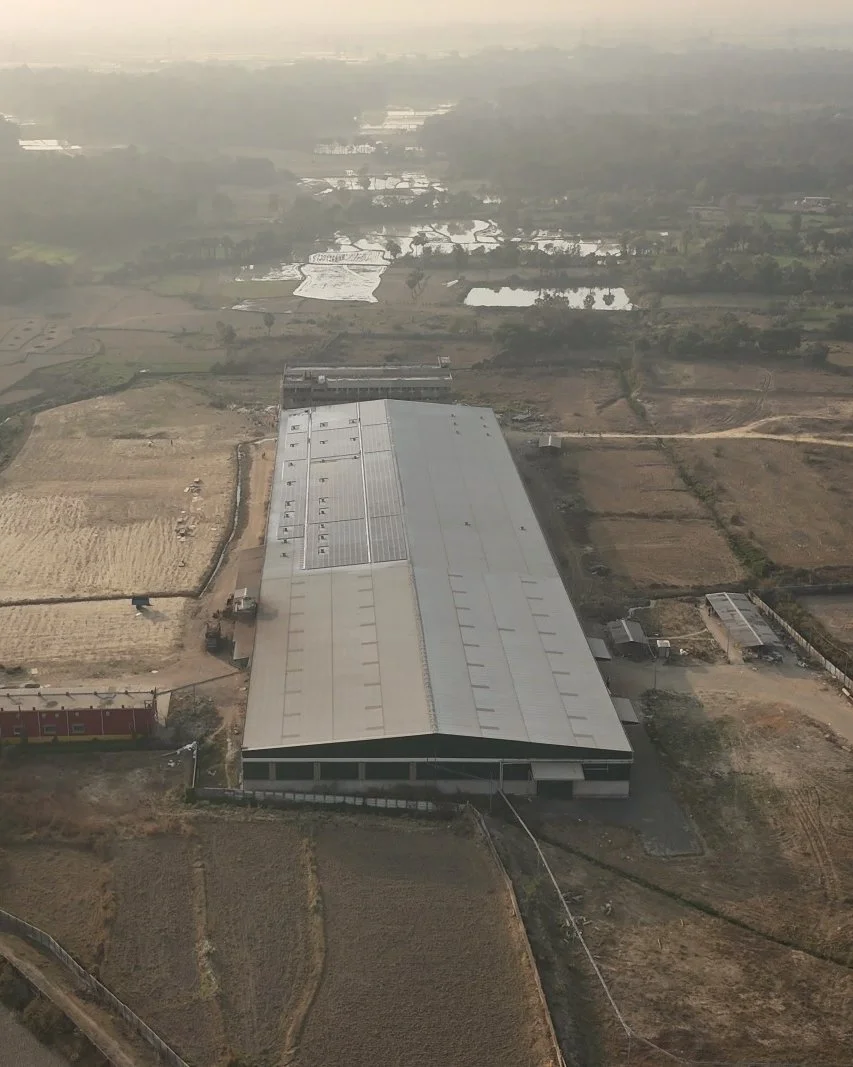 Aerial view of a large industrial building with a metal roof, surrounded by farmland, with ponds and fields in the background.