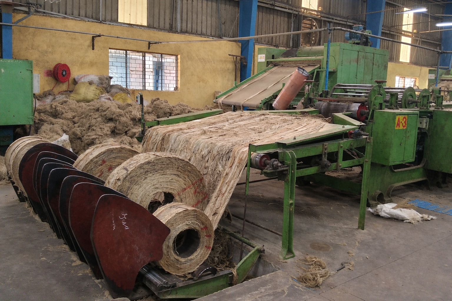 Industrial machine in a factory with rolls of fabric and textile materials around it.
