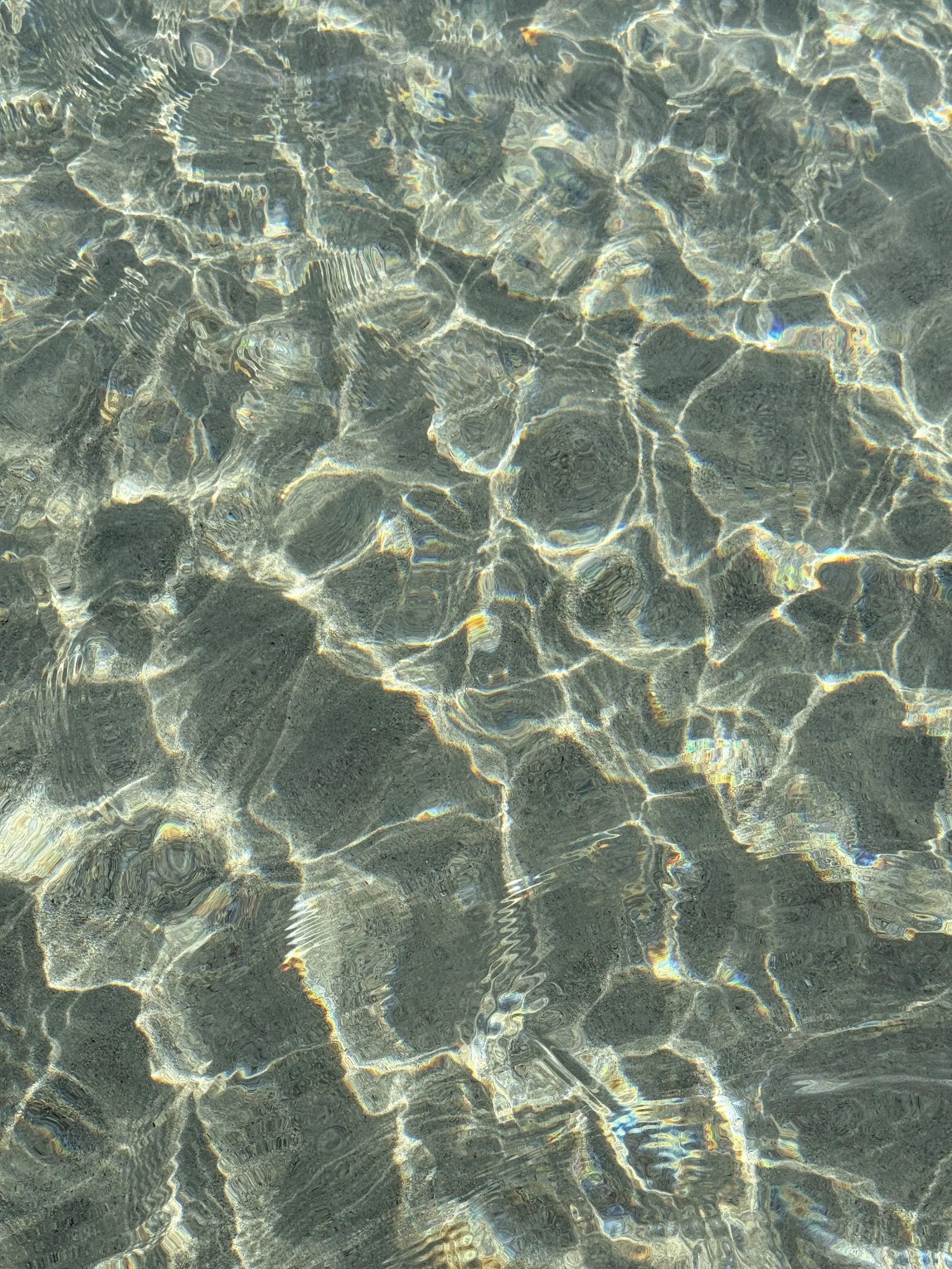 Clear water with sunlight creating shimmering reflections on the sandy bottom.