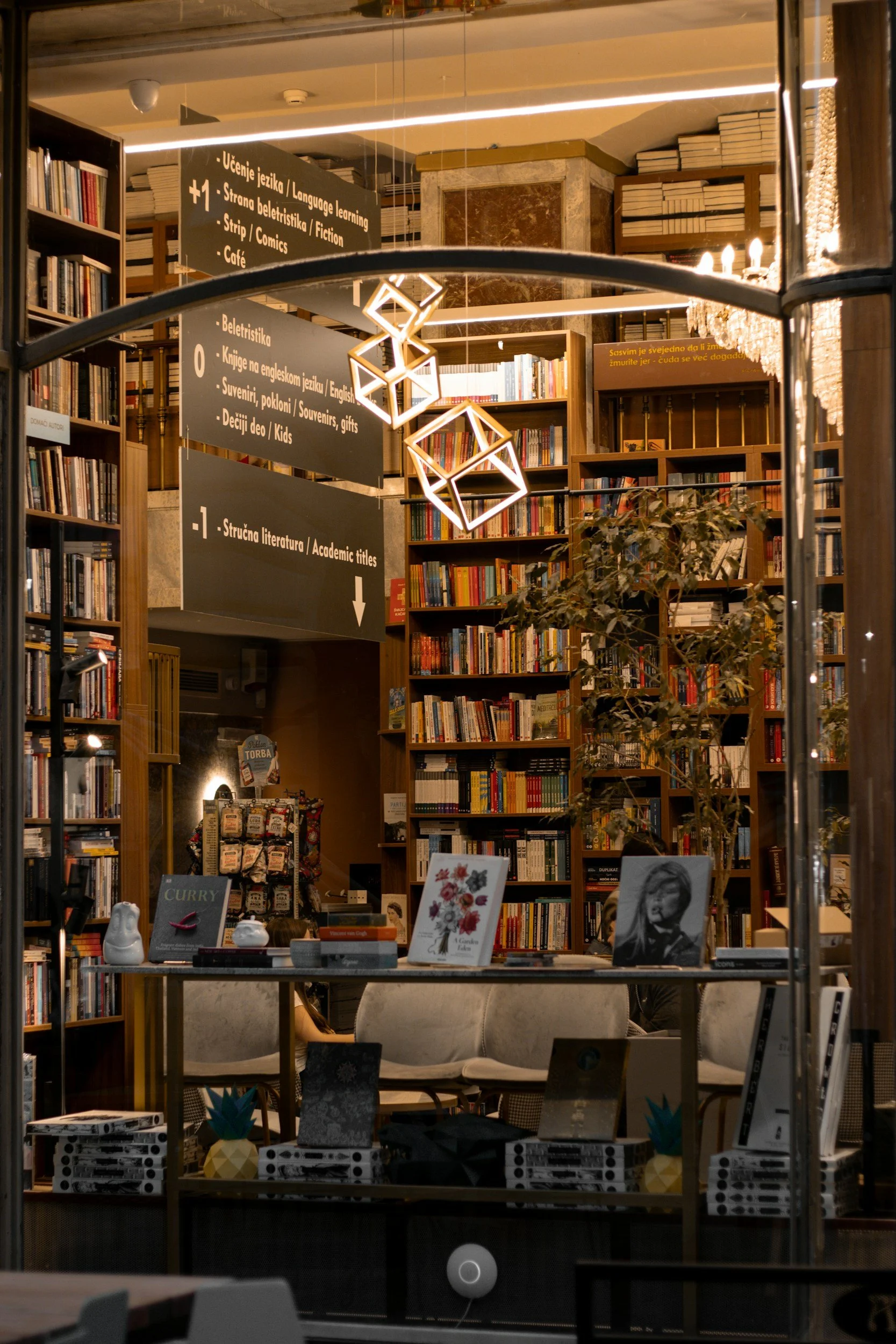 Inside a bookstore with shelves full of books, a hanging geometric light fixture, and a table with books and decor.