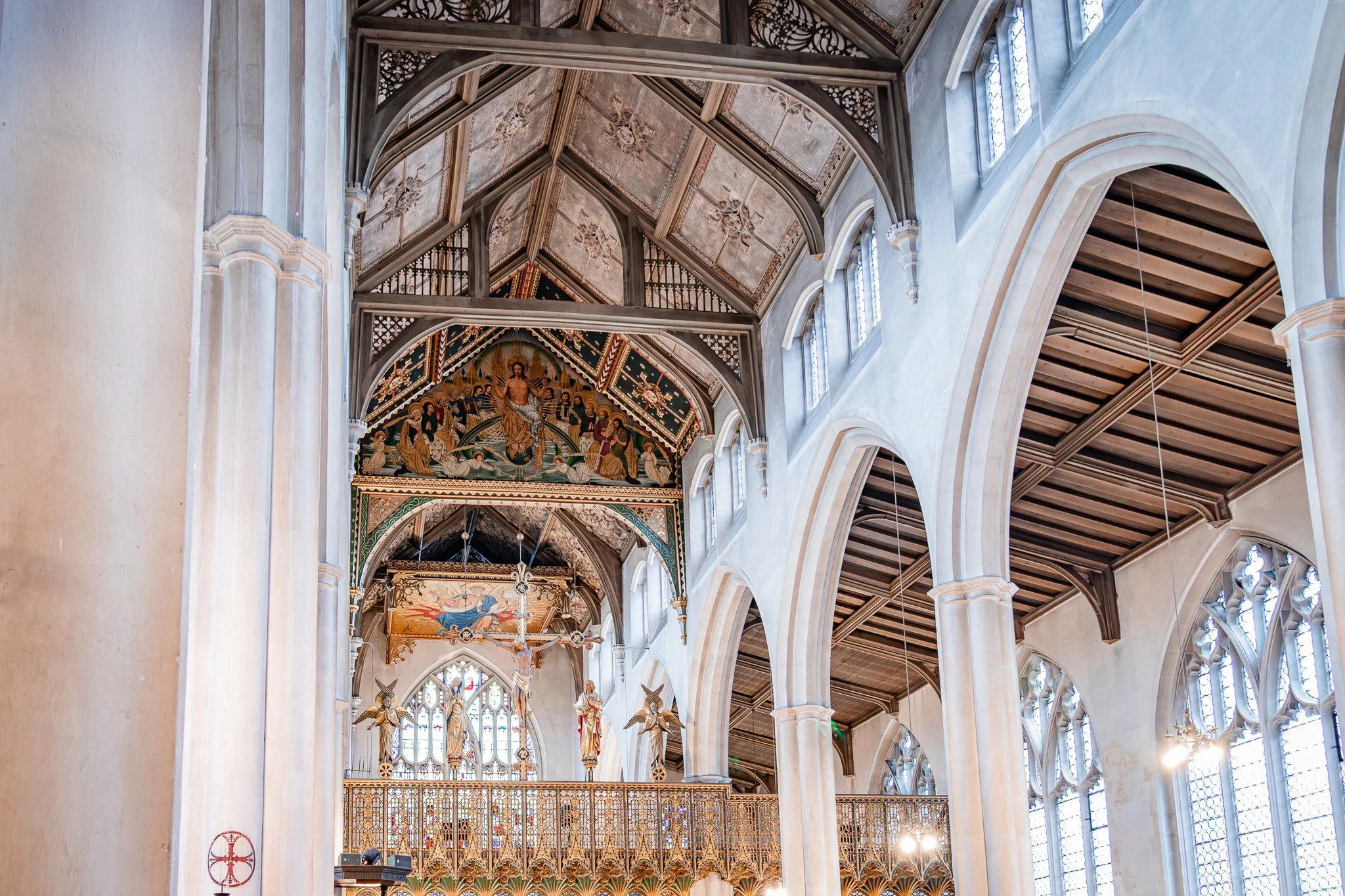 Interior of a church or cathedral with high vaulted ceilings, large stained glass windows, ornate woodwork, and religious paintings and sculptures.