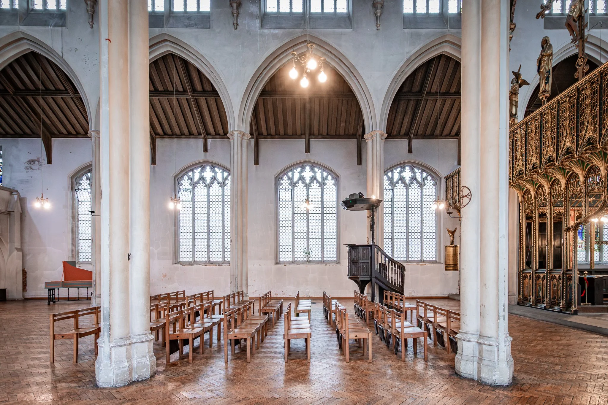Interior of a church with tall arched windows, wooden chairs arranged in rows, and a pulpit in the front. Soaring columns and a vaulted ceiling are visible, with light filtering through the stained glass windows.