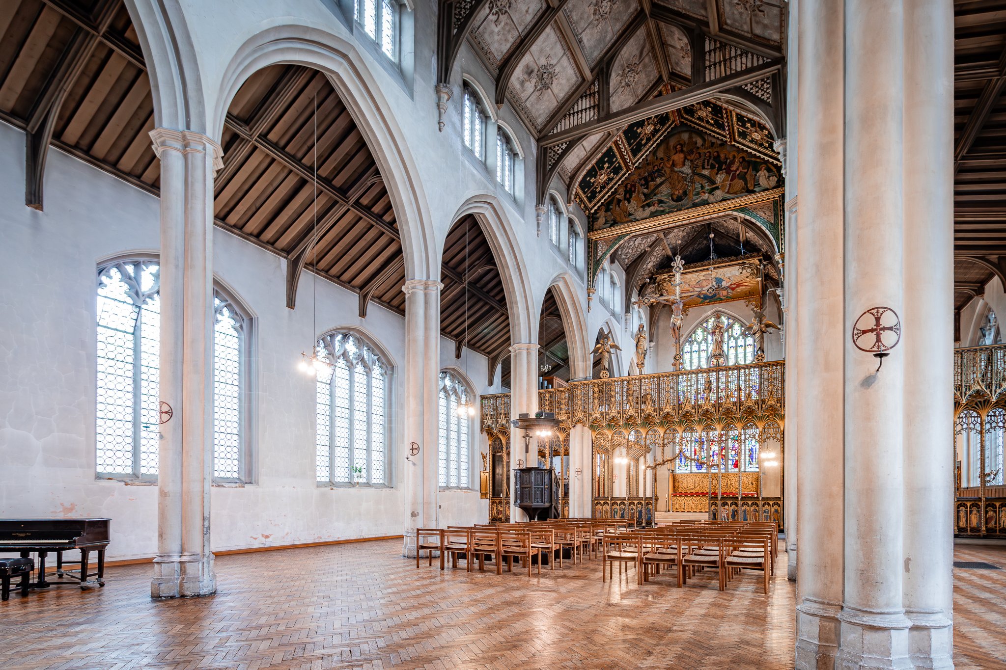Interior of a church with high vaulted ceiling, stained glass windows, wooden pews, and decorative gold accents.