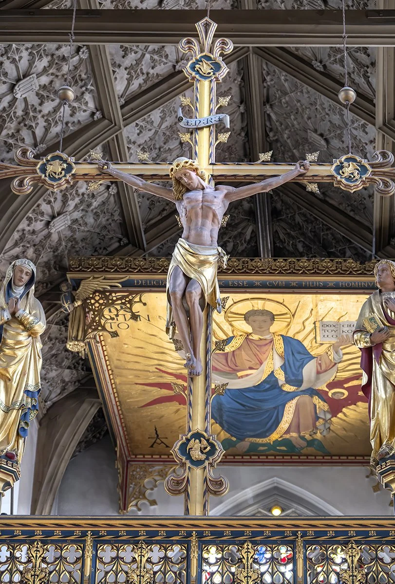 Crucifix with Jesus on the cross, flanked by two statues of saints inside a church, with colorful religious artwork in the background.