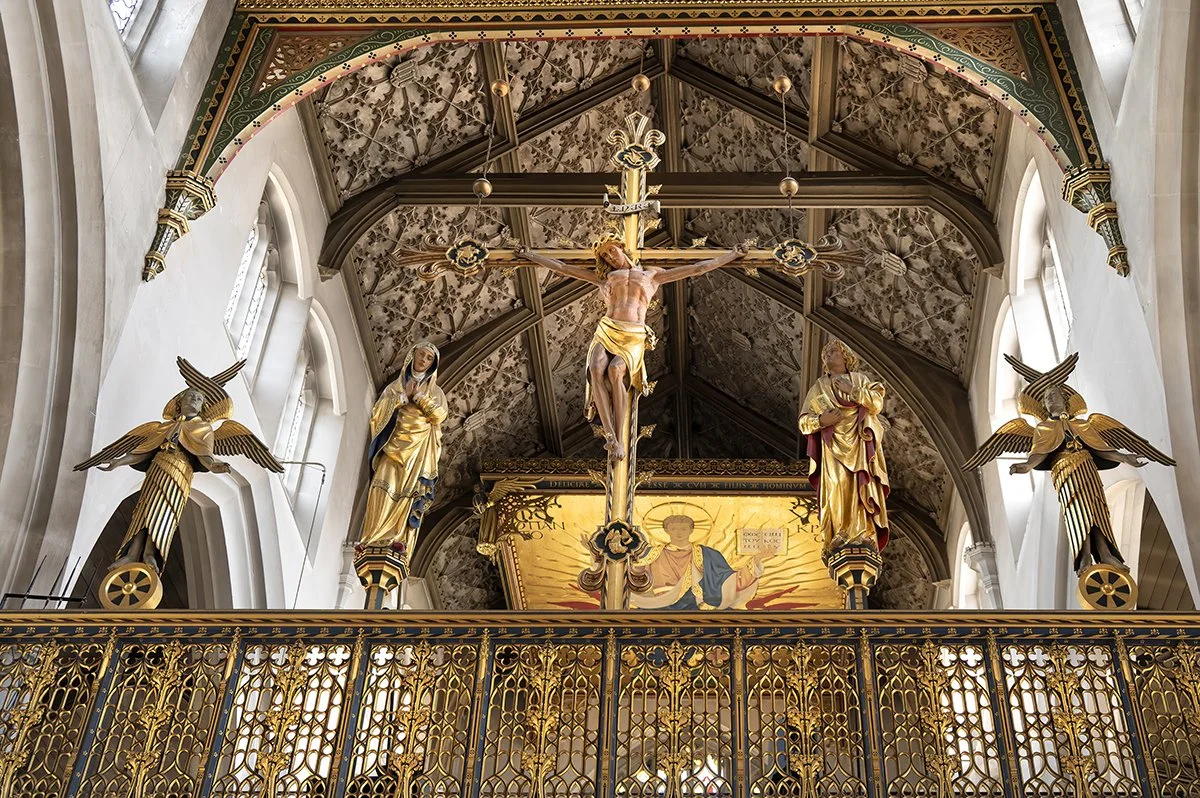 Inside a church, elaborate gold and white religious statues including Jesus on the cross and surrounding figures, with ornate ceiling and decorative railing.