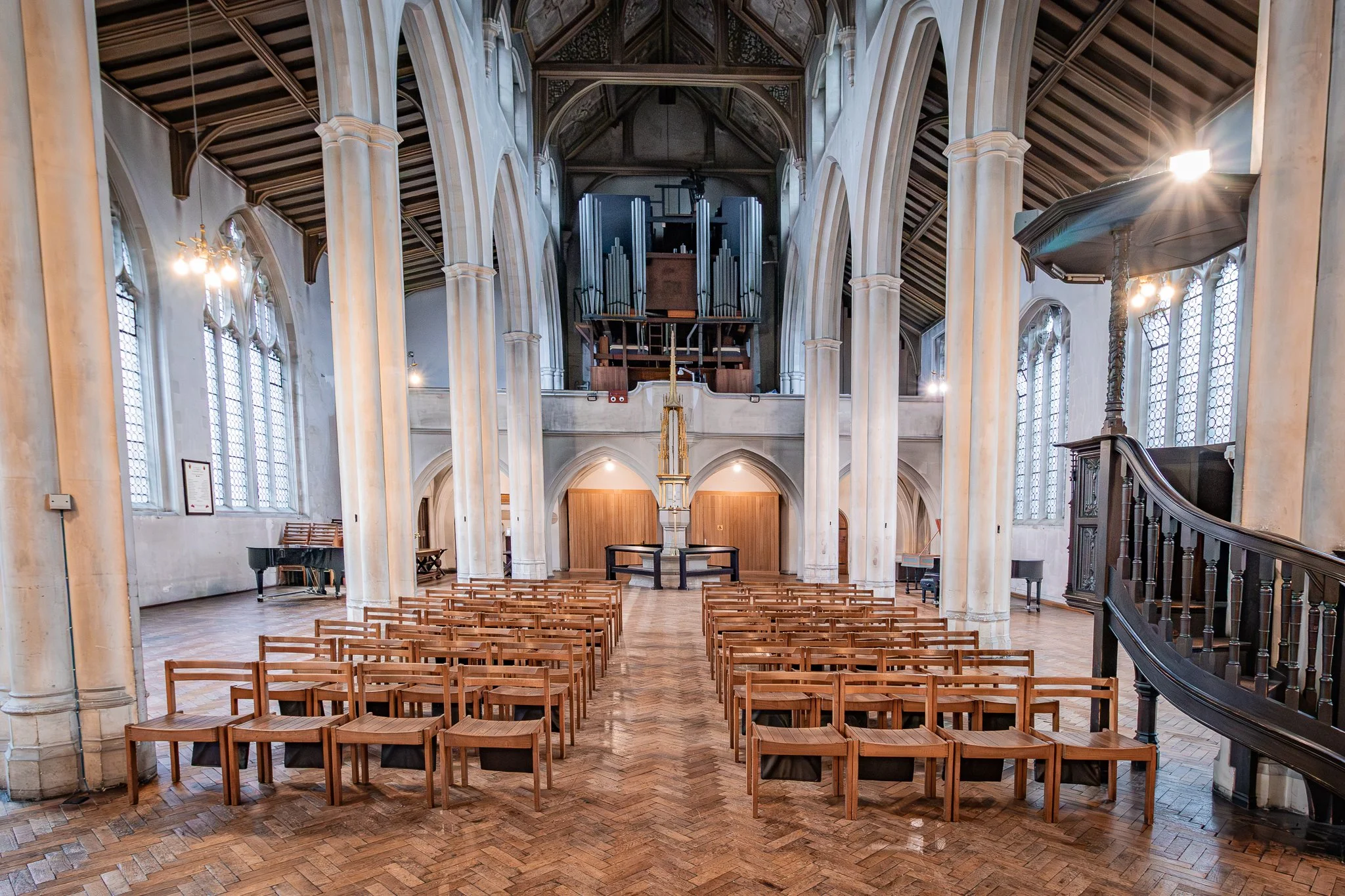 Interior of a church with wooden chairs arranged for a service, large stained glass windows, high vaulted ceiling, organ at the front, and a pulpit on the right.