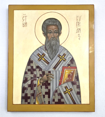 Religious icon of a saint with a halo, wearing a patterned robe, holding a book and a cross, with Greek inscriptions around.