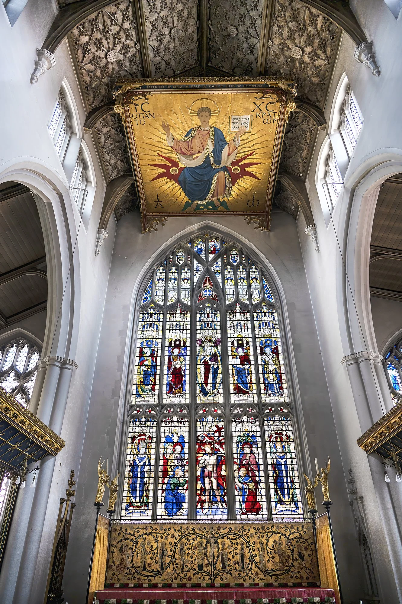 View of a church interior with stained glass windows depicting biblical figures and a ceiling painting of Jesus Christ surrounded by gold rays.
