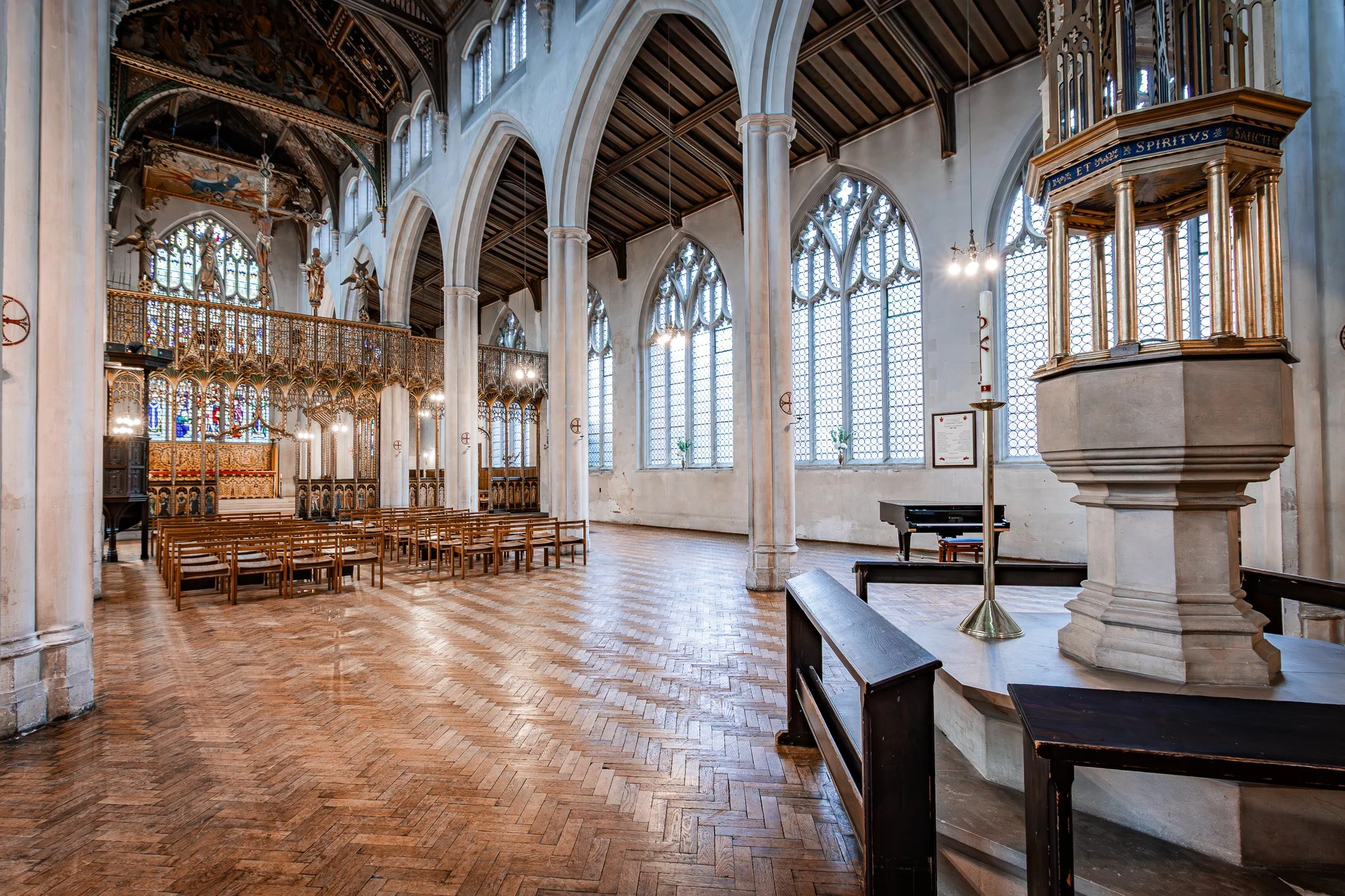 Interior of a historic church with tall, arched windows, wooden pews, an ornate altar, a pulpit, and a piano.