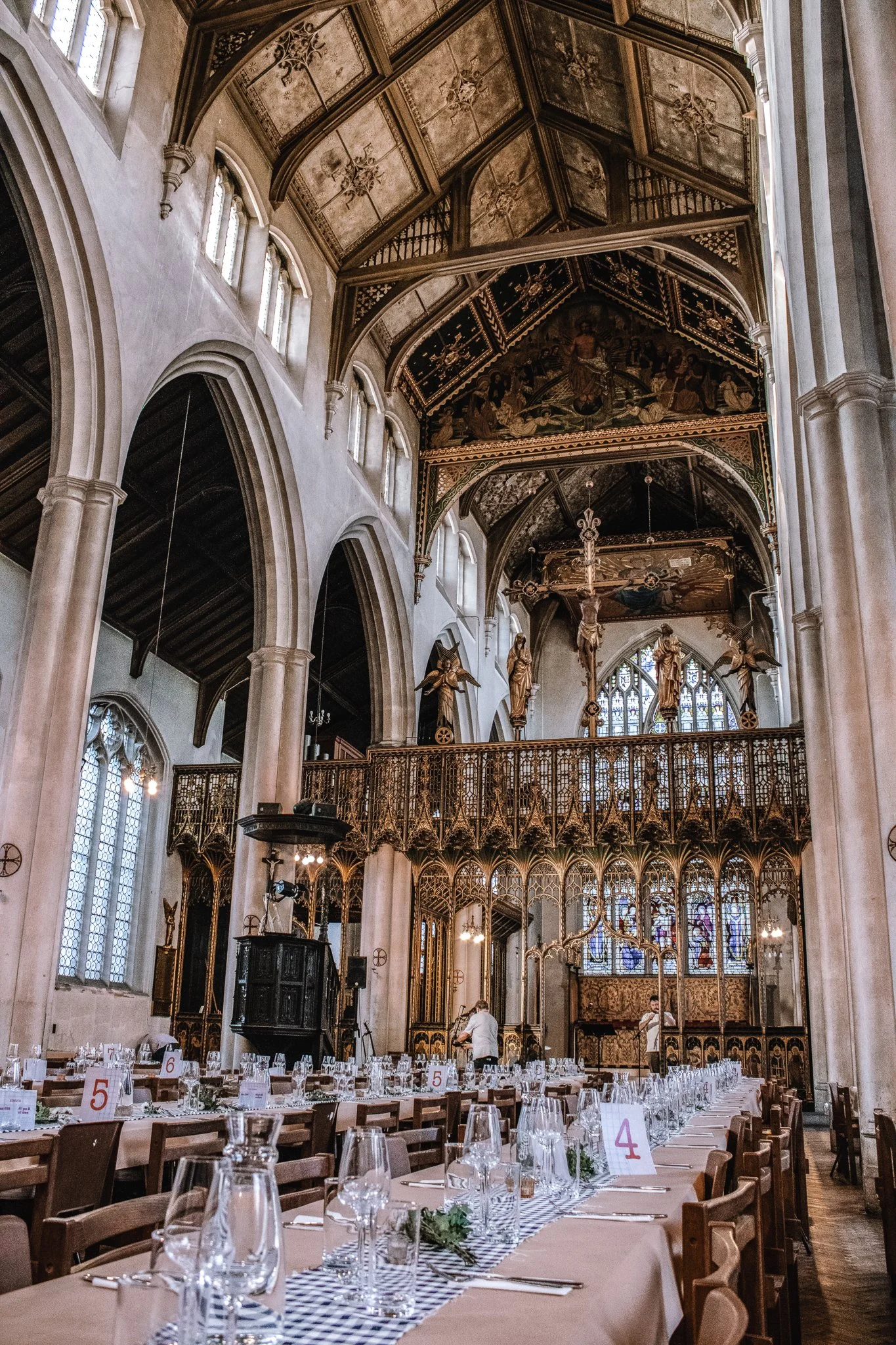 Long banquet table set for an event inside a historic church with ornate architecture, stained glass windows, and tall arches.
