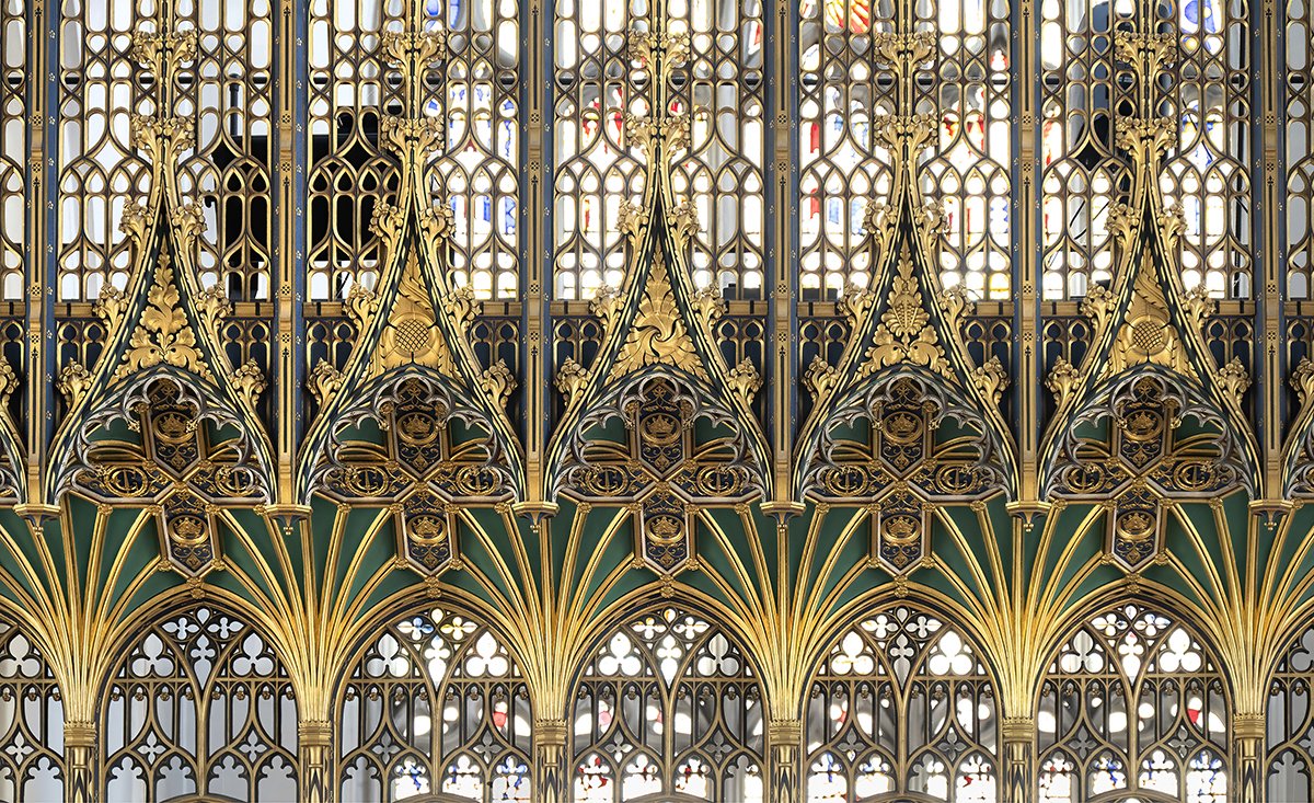 Intricate gold and green metalwork on a cathedral or church facade with stained glass windows in the background.