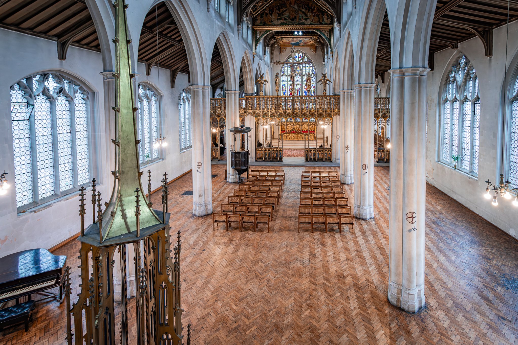 Interior view of a church with wooden pews, high stained glass windows, and an ornate altar area at the front.