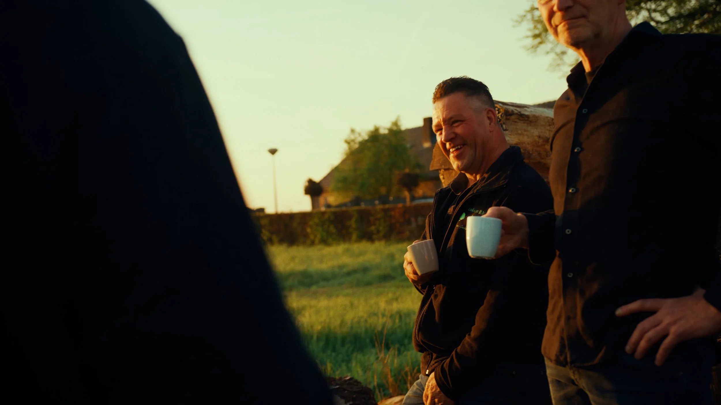 Twee mannen die samen buiten koffie drinken tijdens zonsondergang.