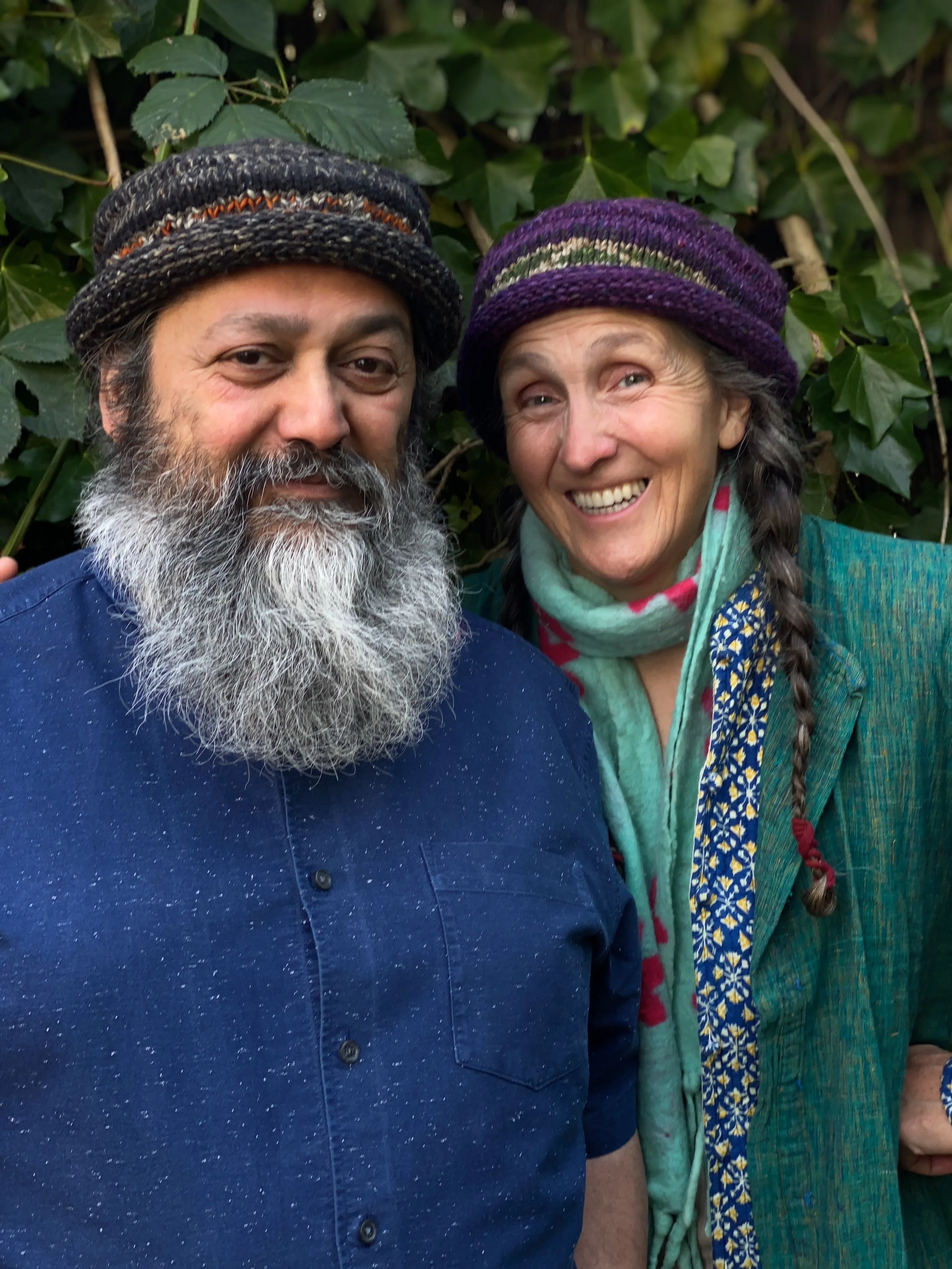 Older man wit a beard in a blue shirt and a woman with a braid birth wearing wool hats