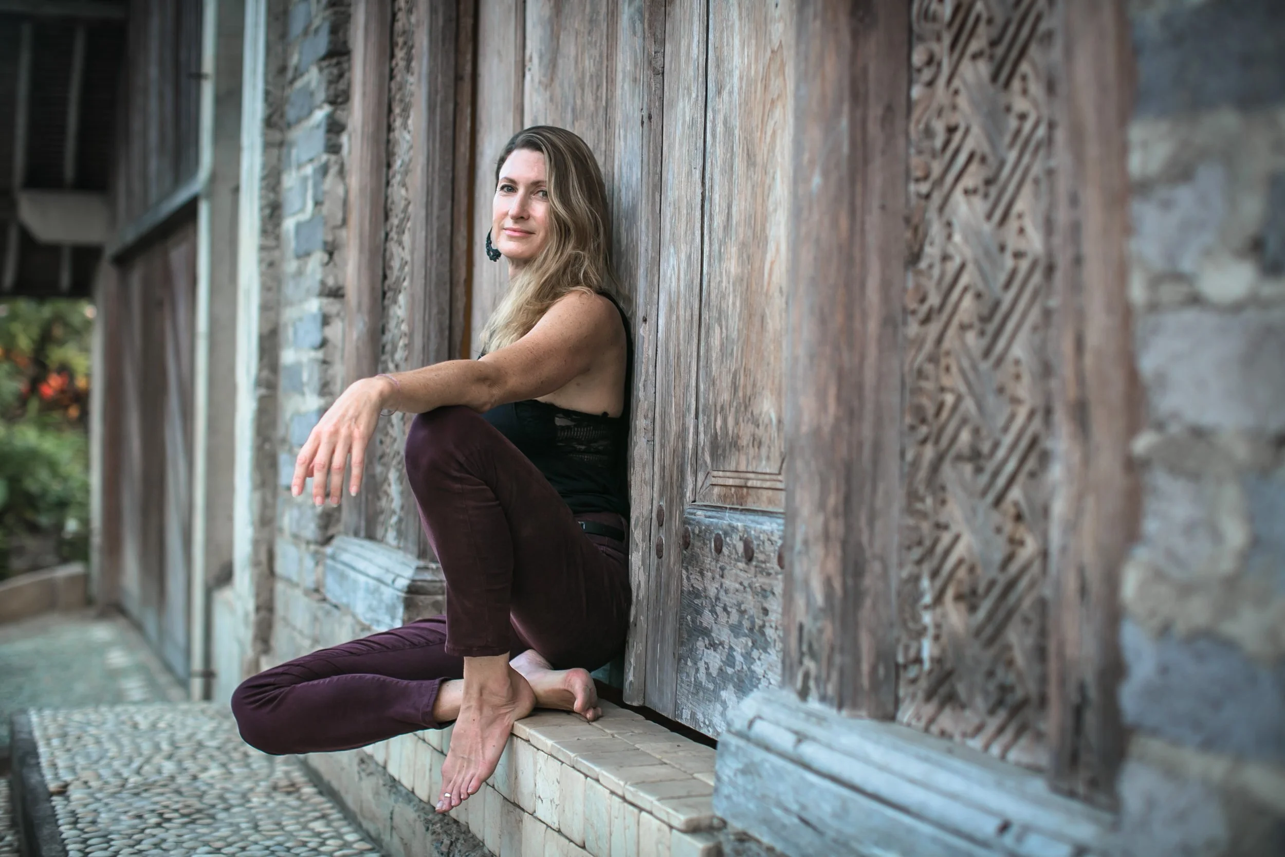 Woman sitting against a wooden door with long hair looking into the camera
