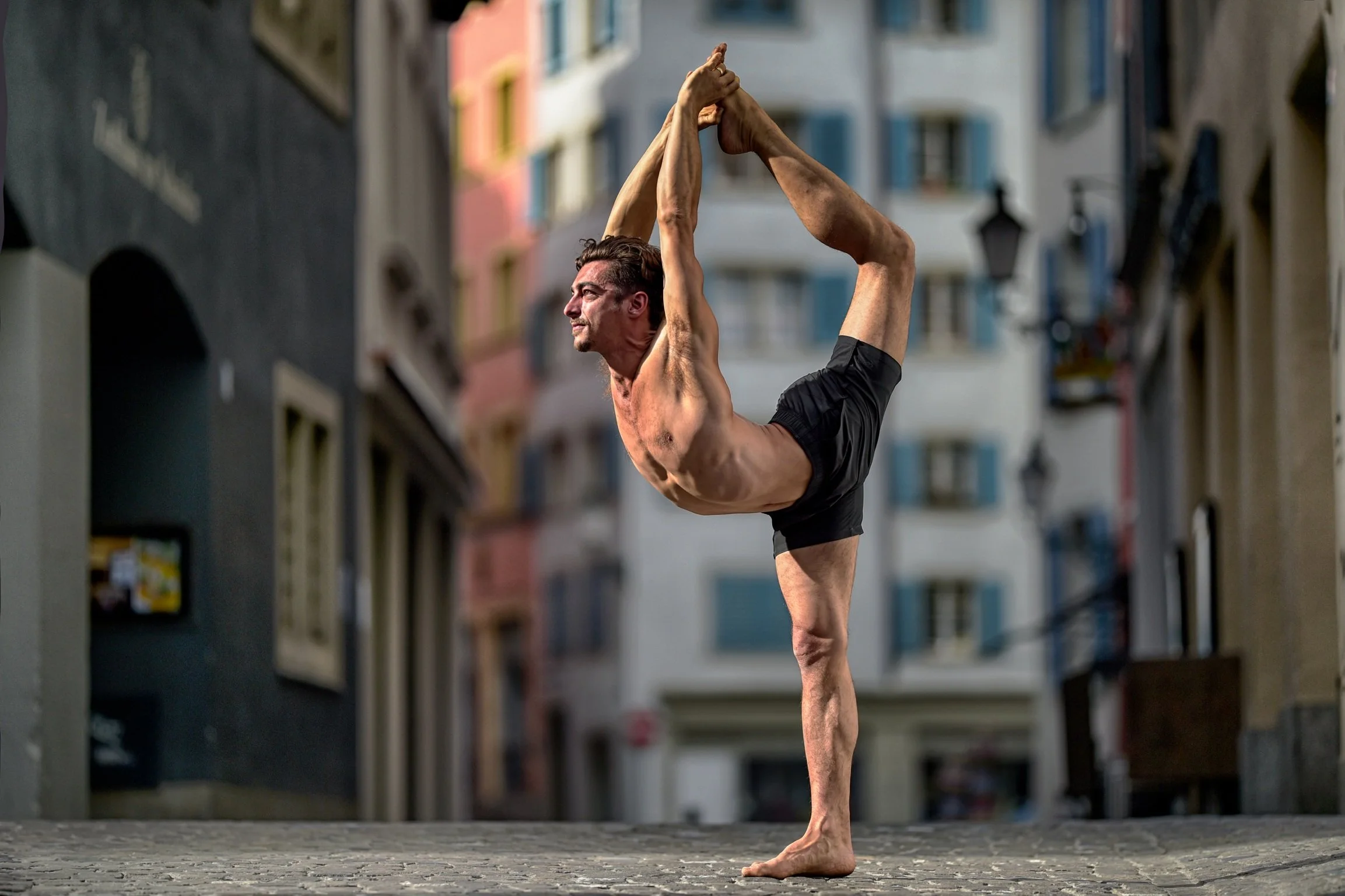 Man in yoga pose in a city with a bear chest wearing shorts