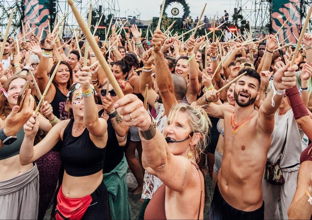 Crowd of people at a festival or concert holding up wooden sticks or batons, smiling and enjoying the event.