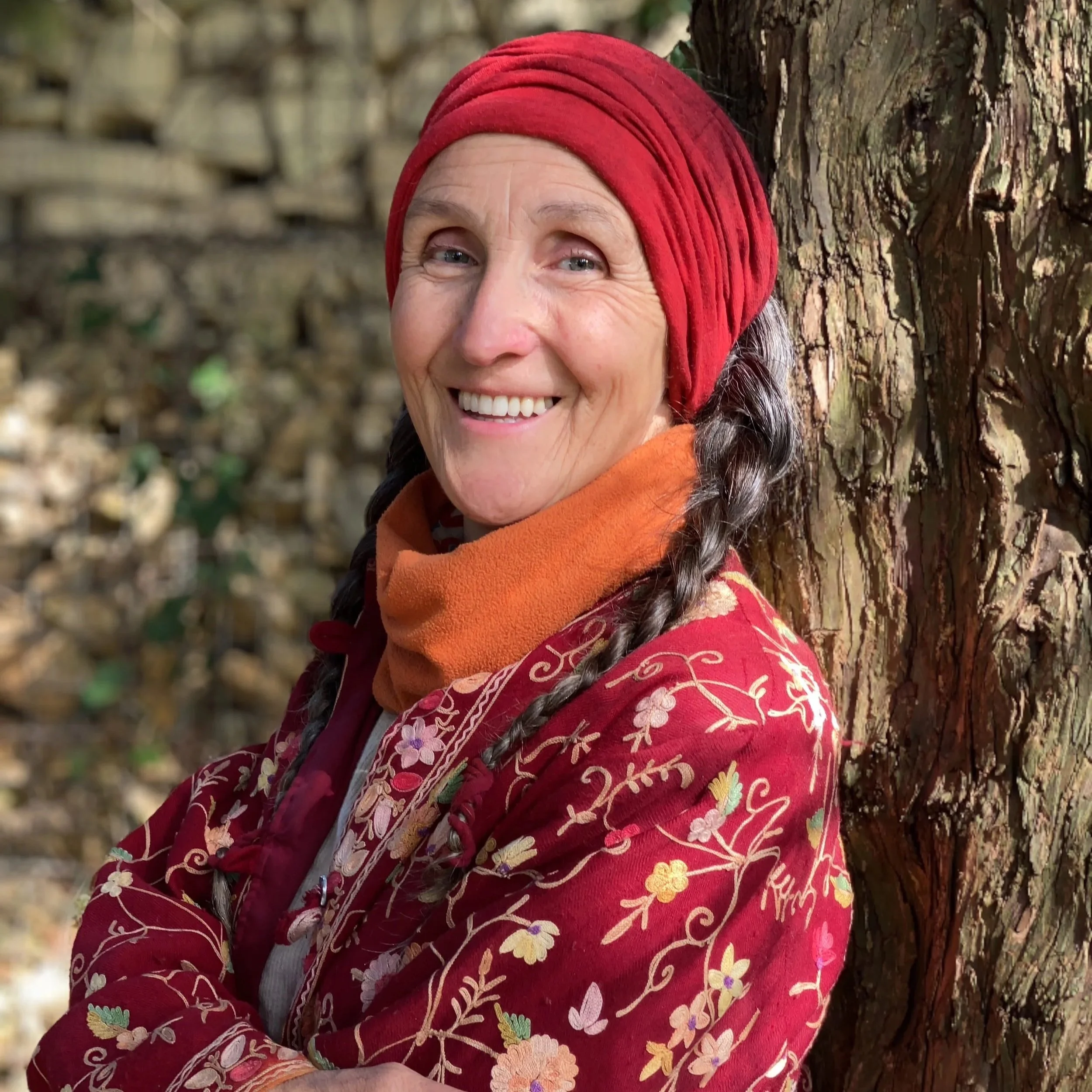 Uma Dinsmore Tuli yoga nidra teacher dressed in red leaning against a tree