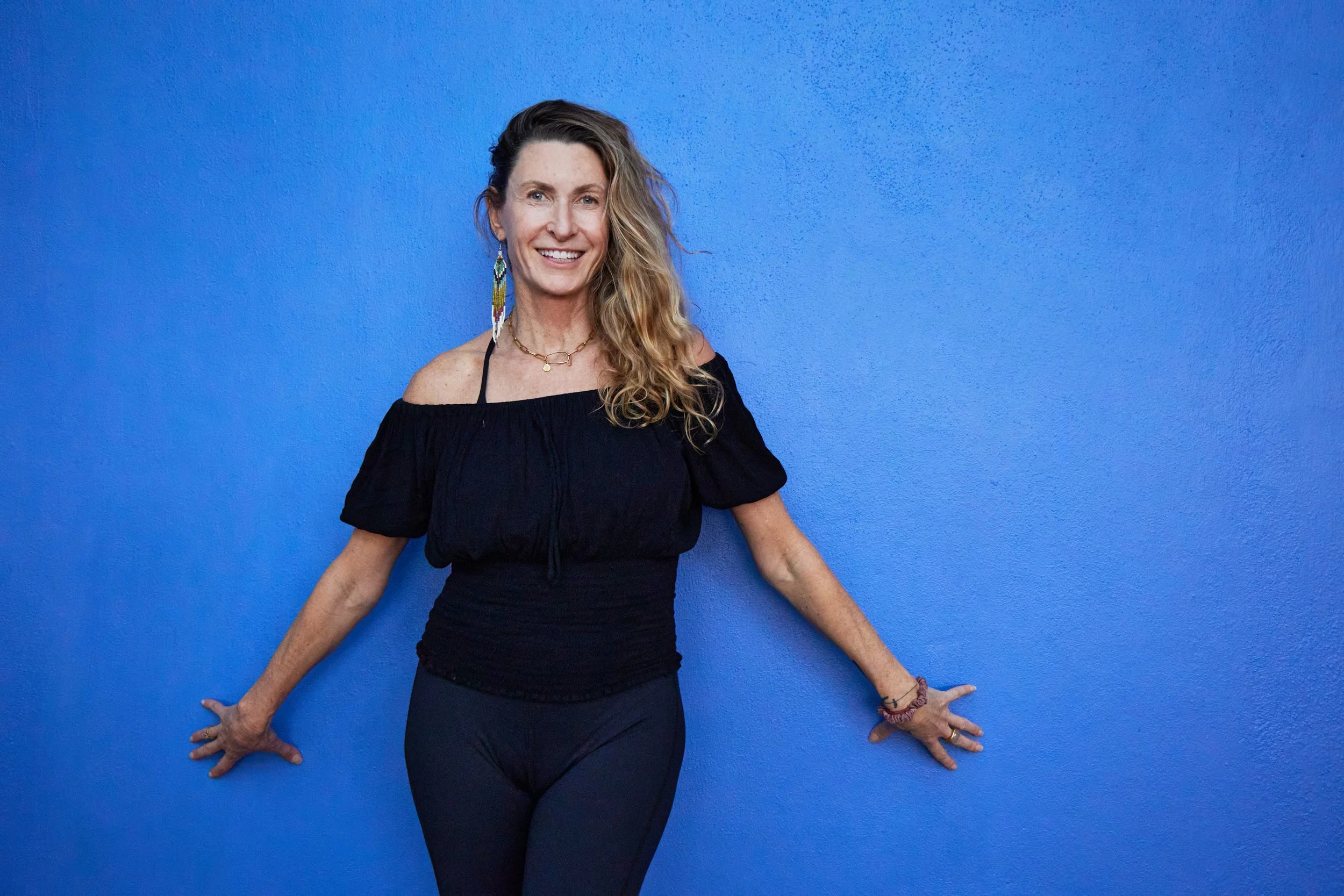 Woman with long hair dressed in black standing against a blue wall