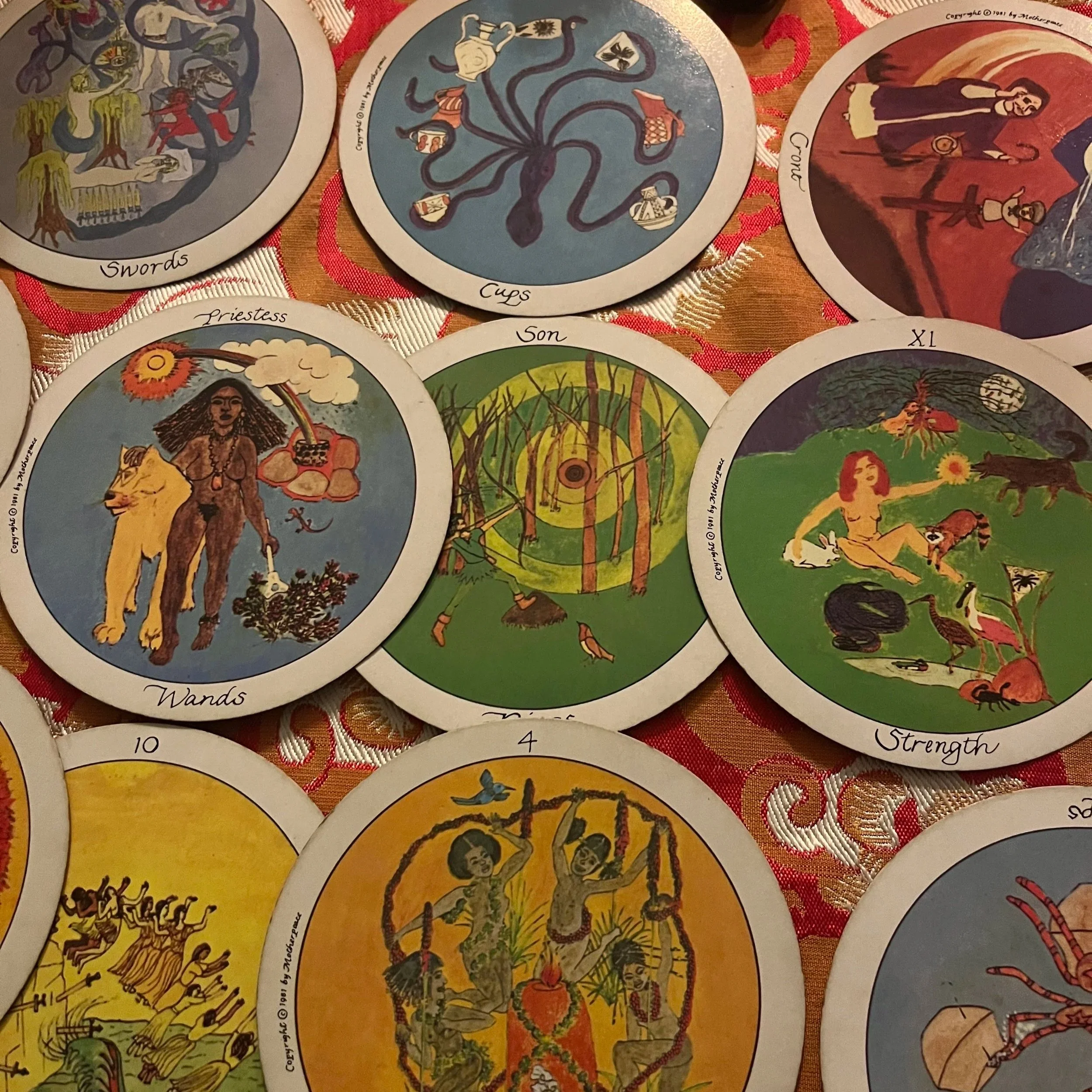 A collection of tarot cards laid out on a patterned fabric. The cards depict various illustrations including a woman with a lion, a forest scene, and a woman with animals, each with a label such as 'Wands', 'Son', 'Strength', and others.