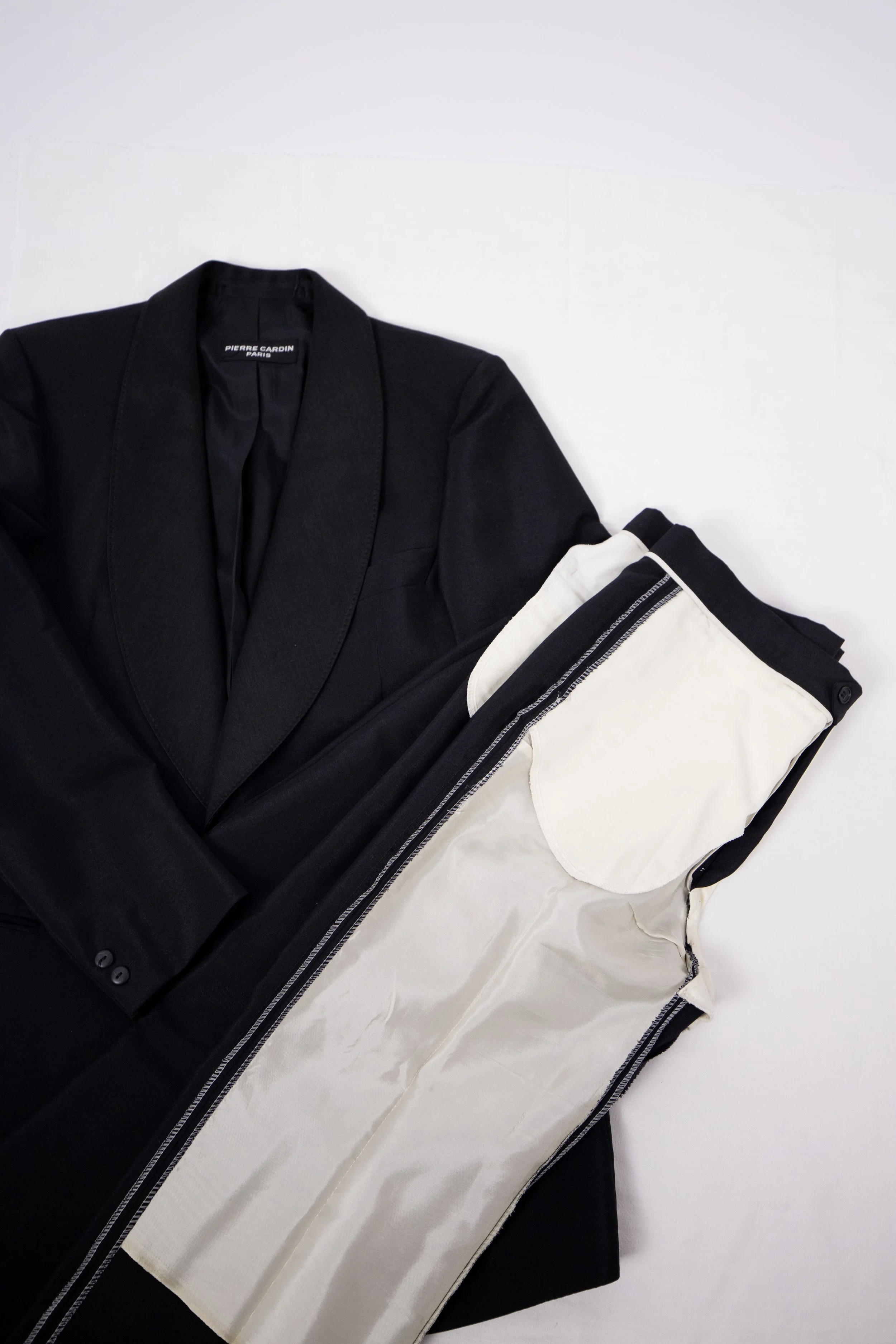 Black blazer and white pants with black waistband and zipper laid out on a white surface.