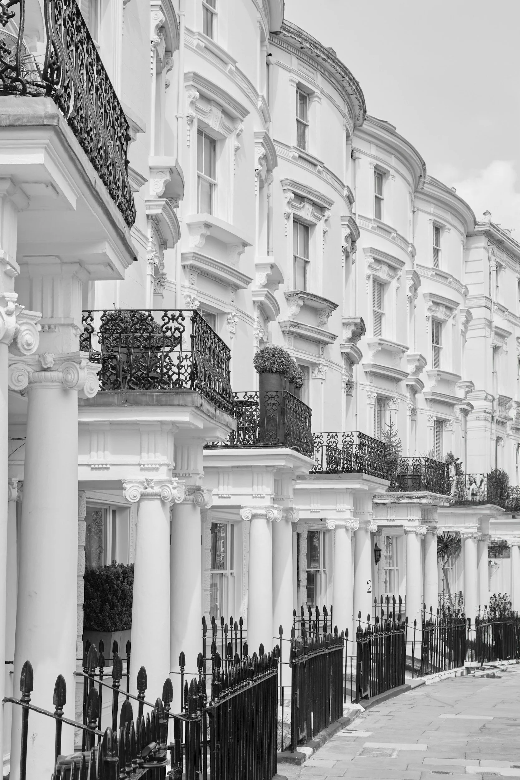 Row of white Victorian-style townhouses with decorative moldings, large windows, and black wrought iron balconies, photographed in black and white.
