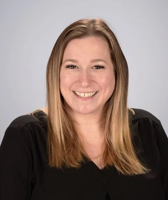 A woman with shoulder-length blonde hair, smiling, wearing a black top against a neutral background.