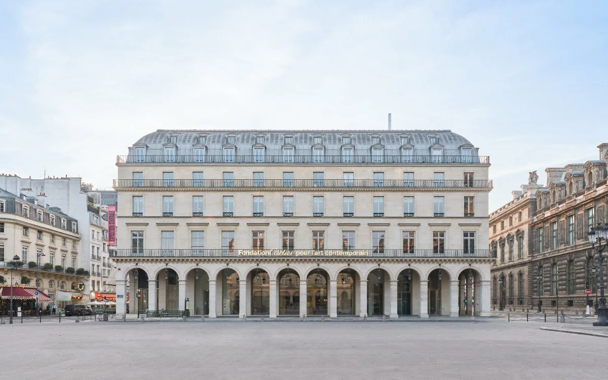 Bâtiment de style parisien avec plusieurs étages, arcades au rez-de-chaussée, et un toit en mansarde en métal