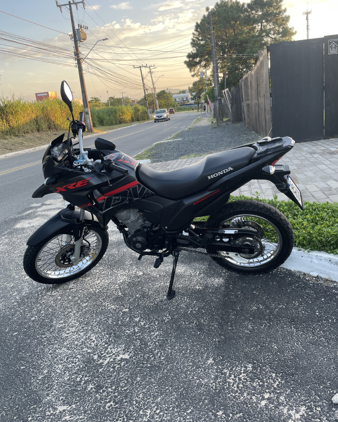 Moto Honda NXR Adventure preta para aluguel em Florianópolis, estacionada em rua urbana ao entardecer.