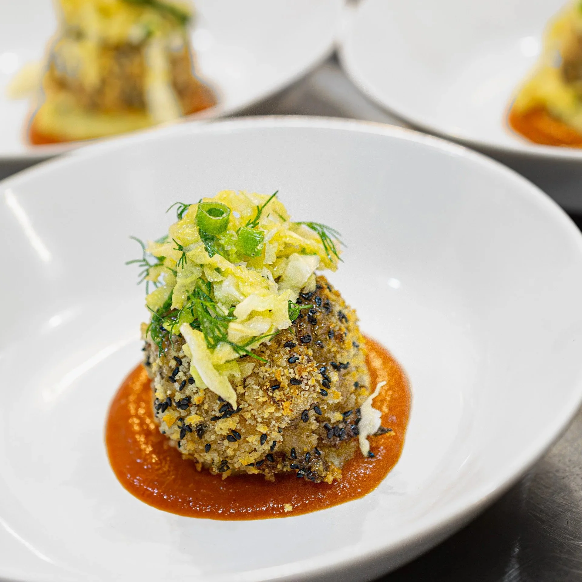 Fried croquette topped with chopped green onions and herbs, served on a bed of red sauce in a white bowl.