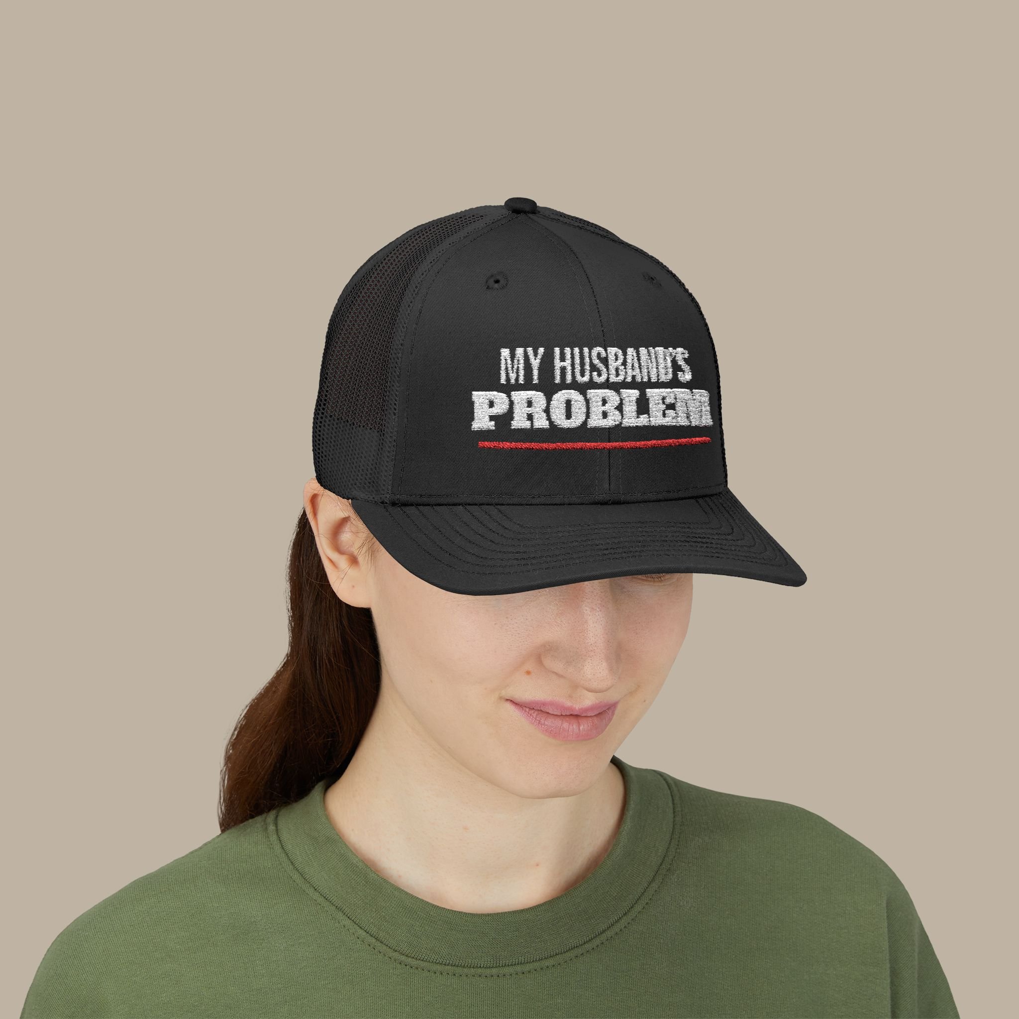 Person wearing the Black My Husband’s Problem trucker hat, showing white embroidery and the red underline.