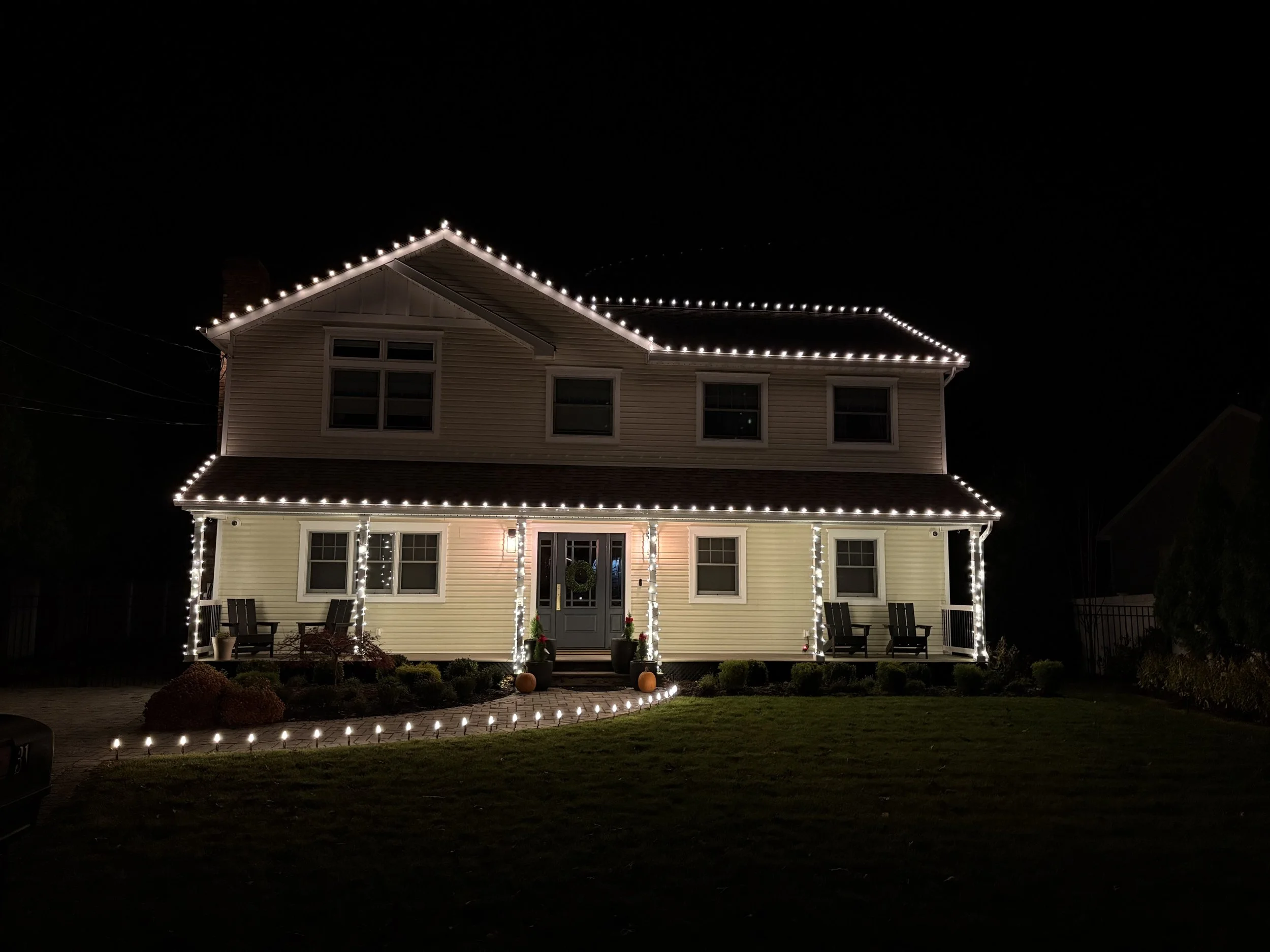 A two-story house decorated with white string lights outlining the roof, front porch, and windows at night.