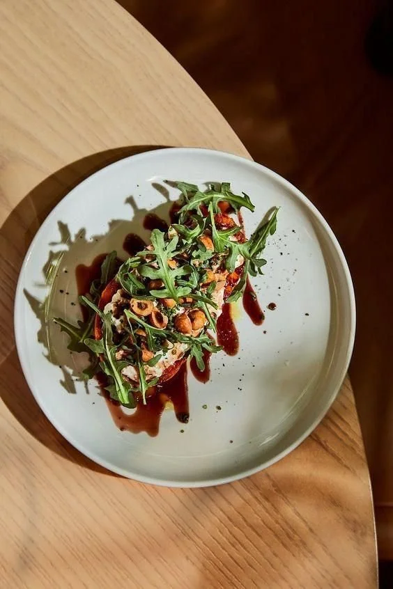 A plate of food garnished with arugula, nuts, and drizzled with balsamic glaze on a wooden table.