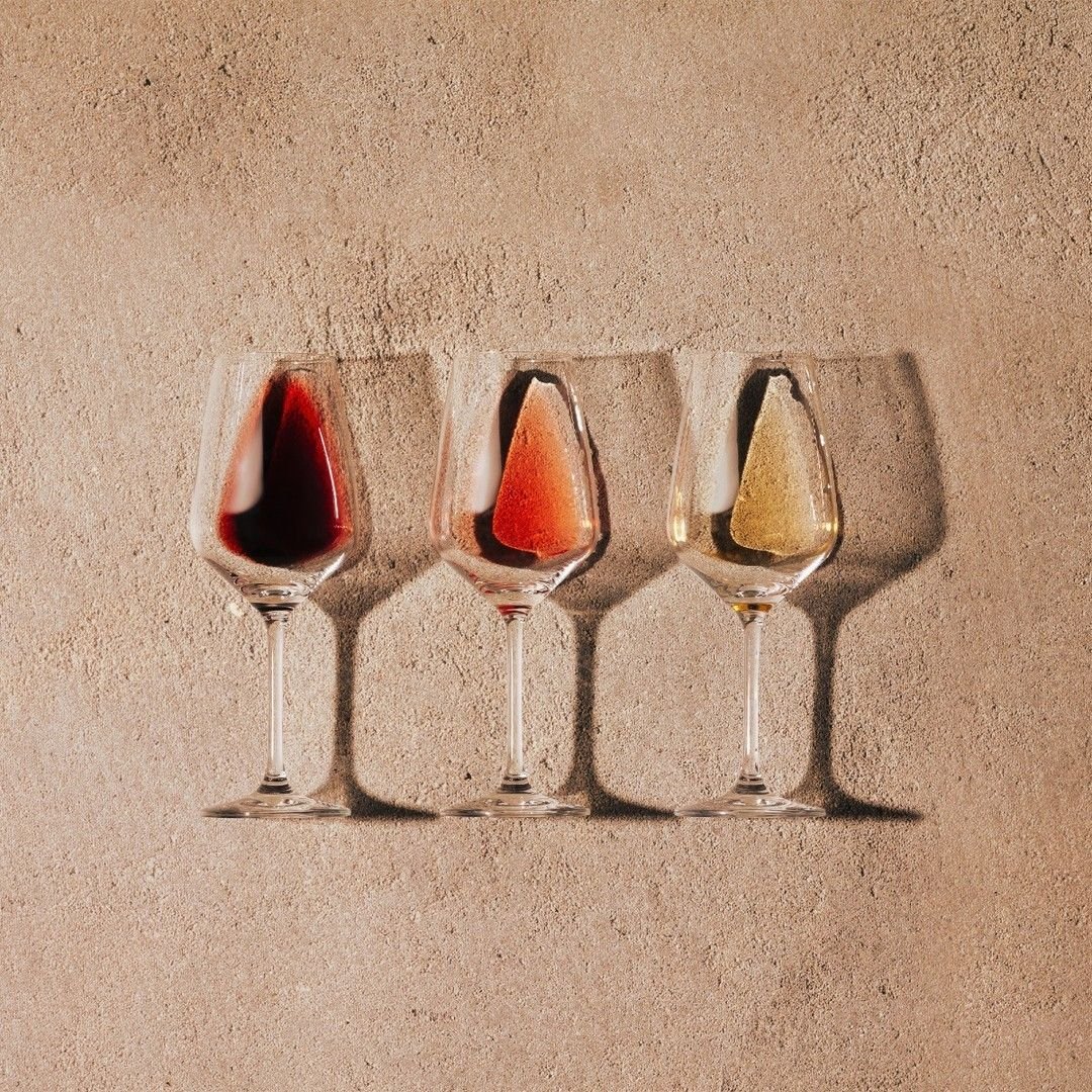 Three wine glasses with wine, casting shadows on a textured beige wall.
