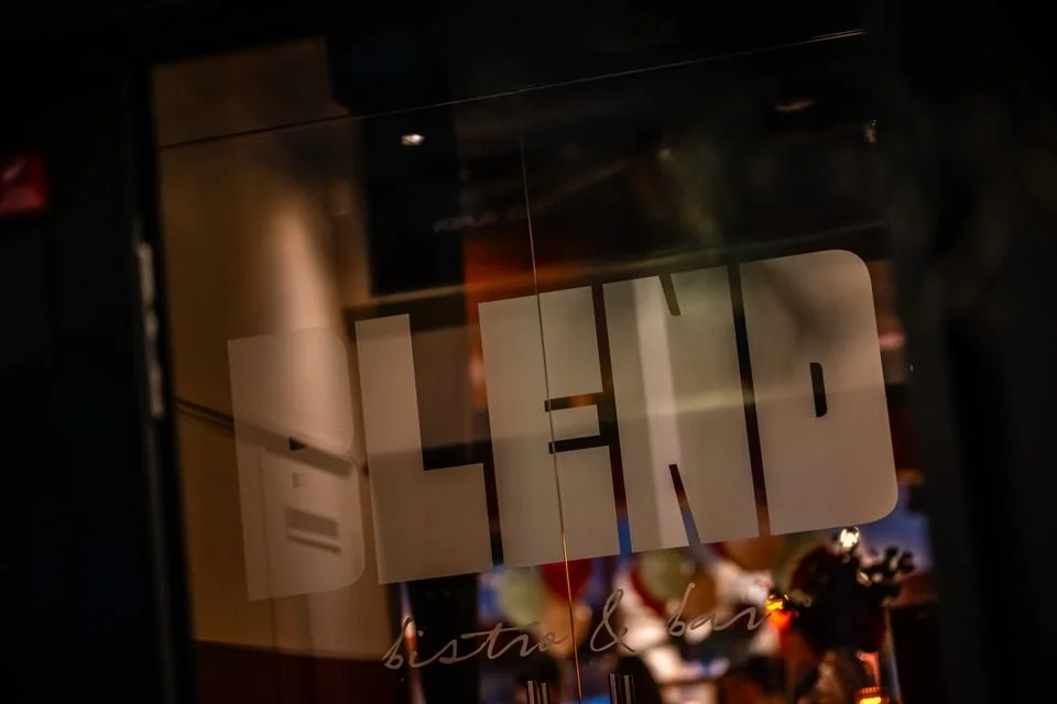 The image shows a glass door with the word 'ELK' in large letters, indicating a restaurant and bar named 'ELK Bistro & Bar,' with reflections and warm indoor lighting visible through the glass.