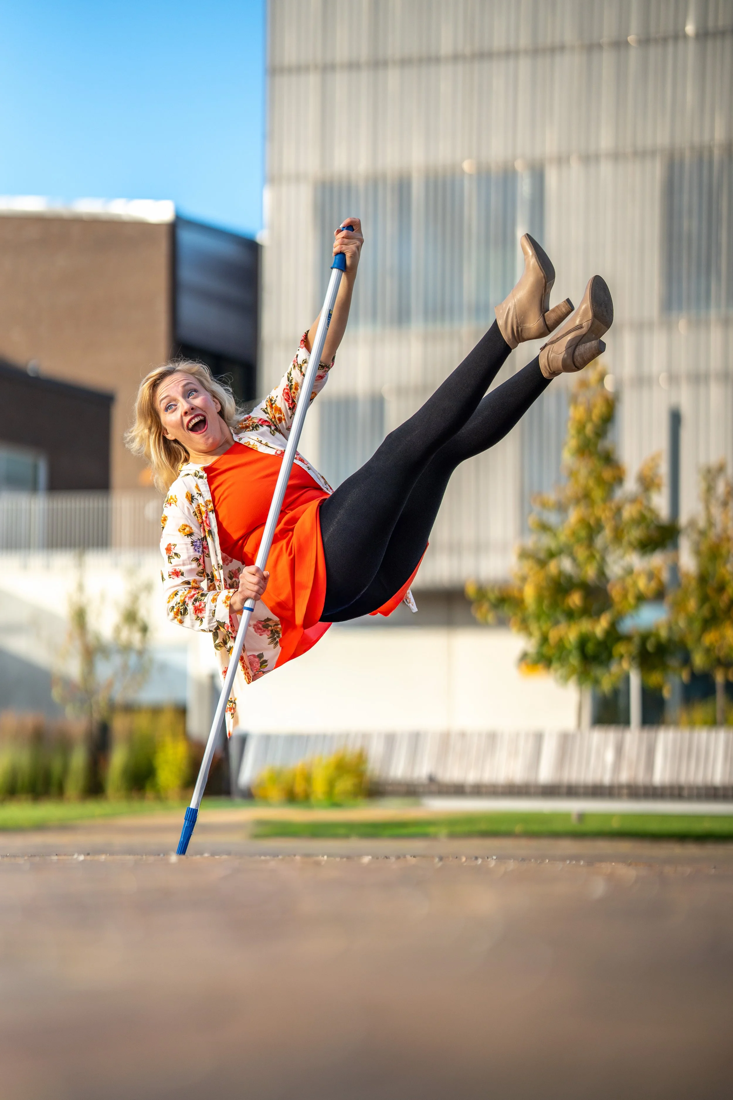 A woman holding a mop and falling upside down with a surprised expression outdoors near a modern building.