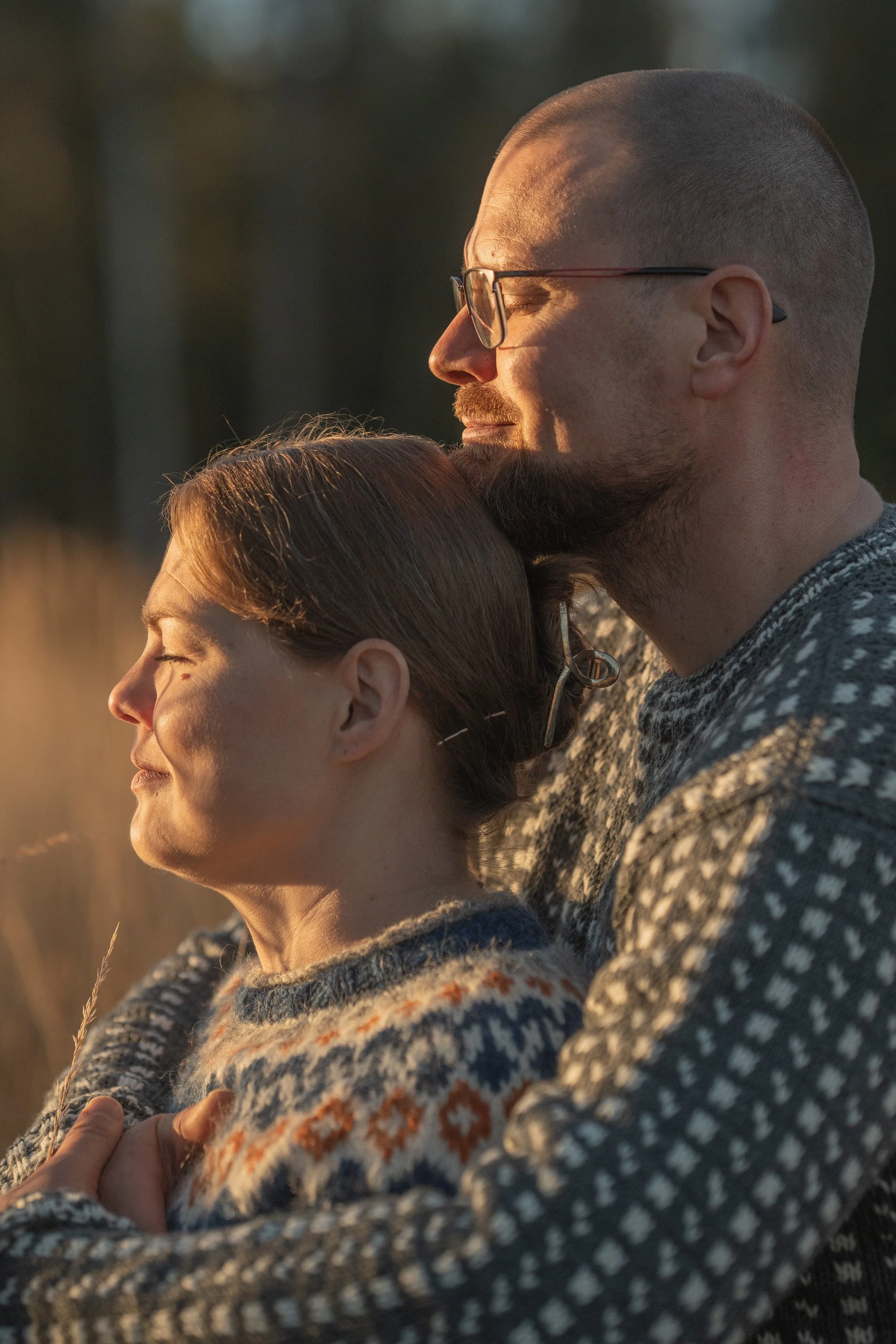 A close-up of a couple standing outdoors in the golden hour sunlight, with their eyes closed, embracing peacefully.