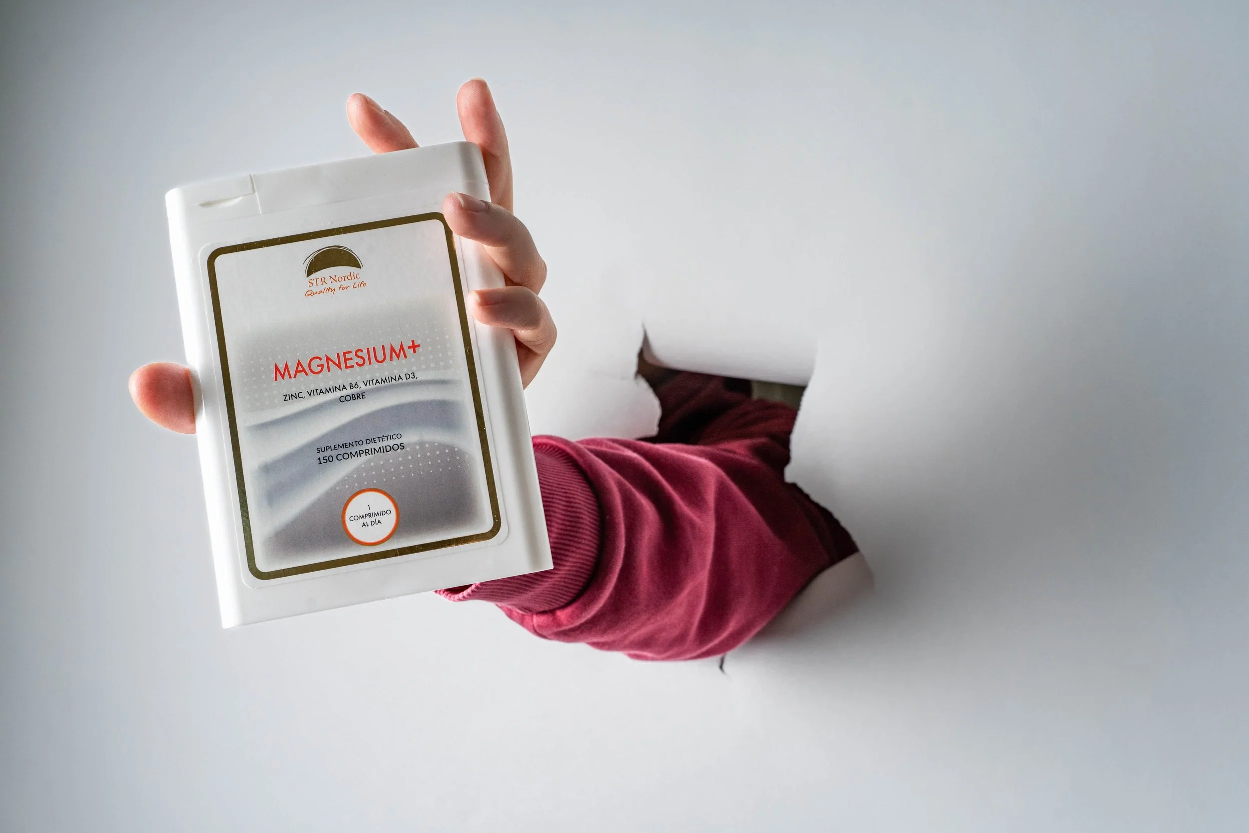 A person wearing a red long sleeve shirt holds a packet of magnesium supplements with a torn background.