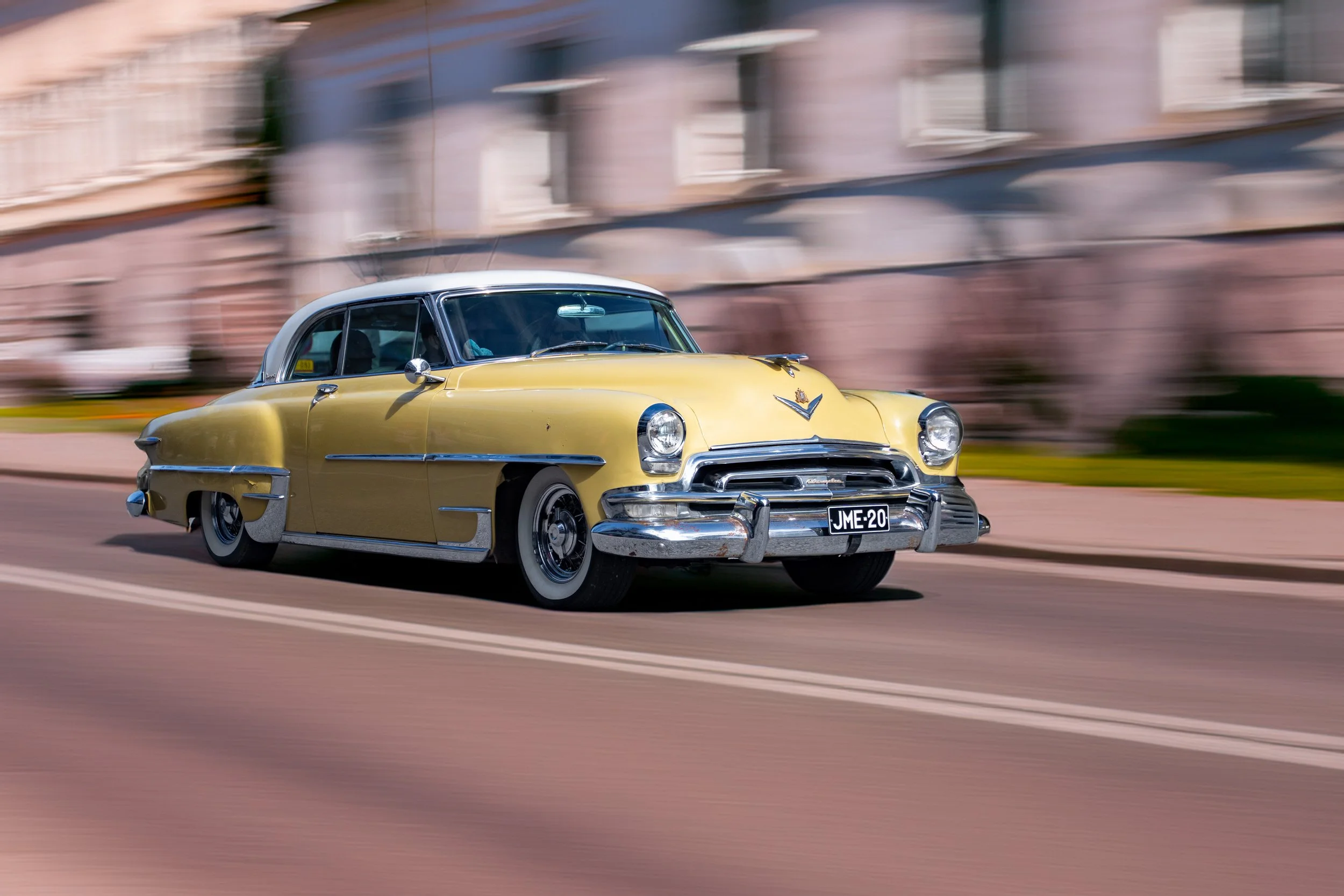 A vintage yellow Cadillac driving on a city street during the day, with motion blur background.