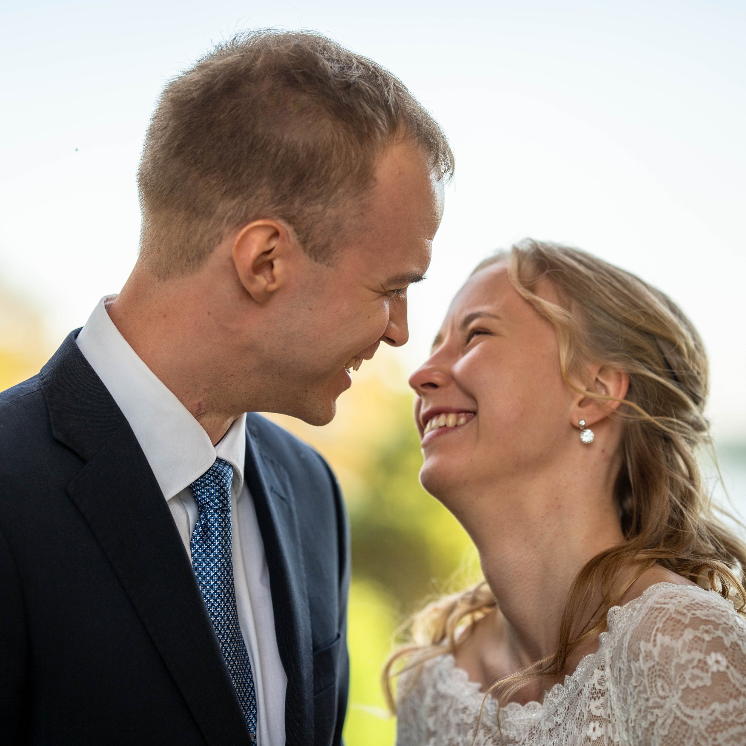 A man and woman share a joyful moment close up, with their faces touching and smiling at each other outdoors.