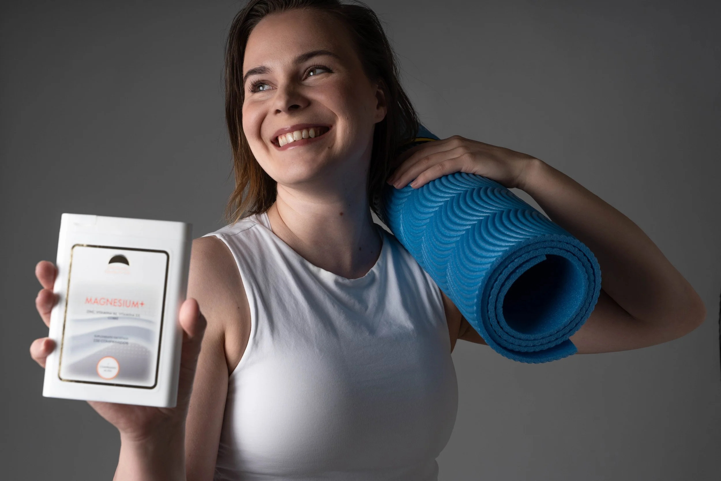 Woman holding a box of magnesium supplement and a rolled blue yoga mat.
