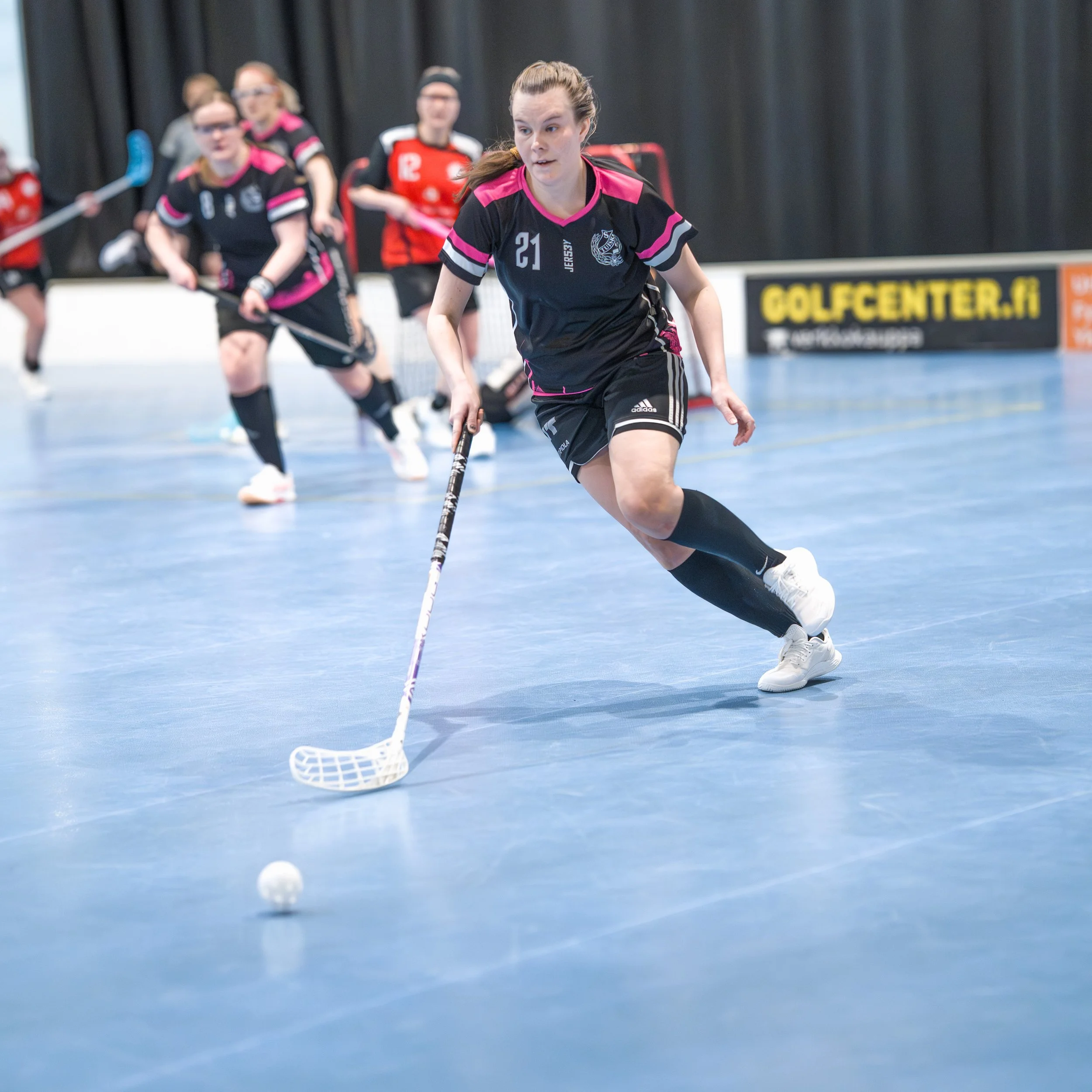 Female floorball player in black and pink uniform controlling the ball during a game.