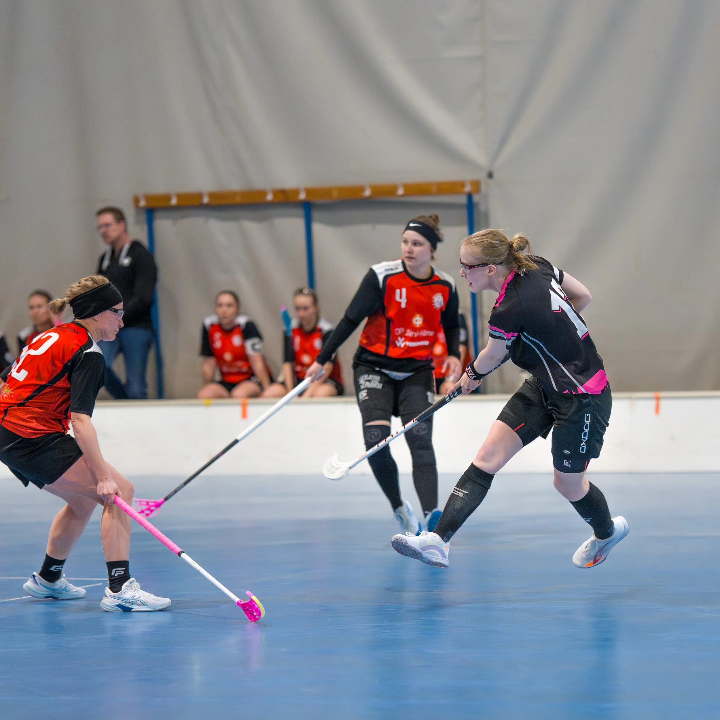 Girls playing floor hockey in an indoor rink with some team members and a coach watching.