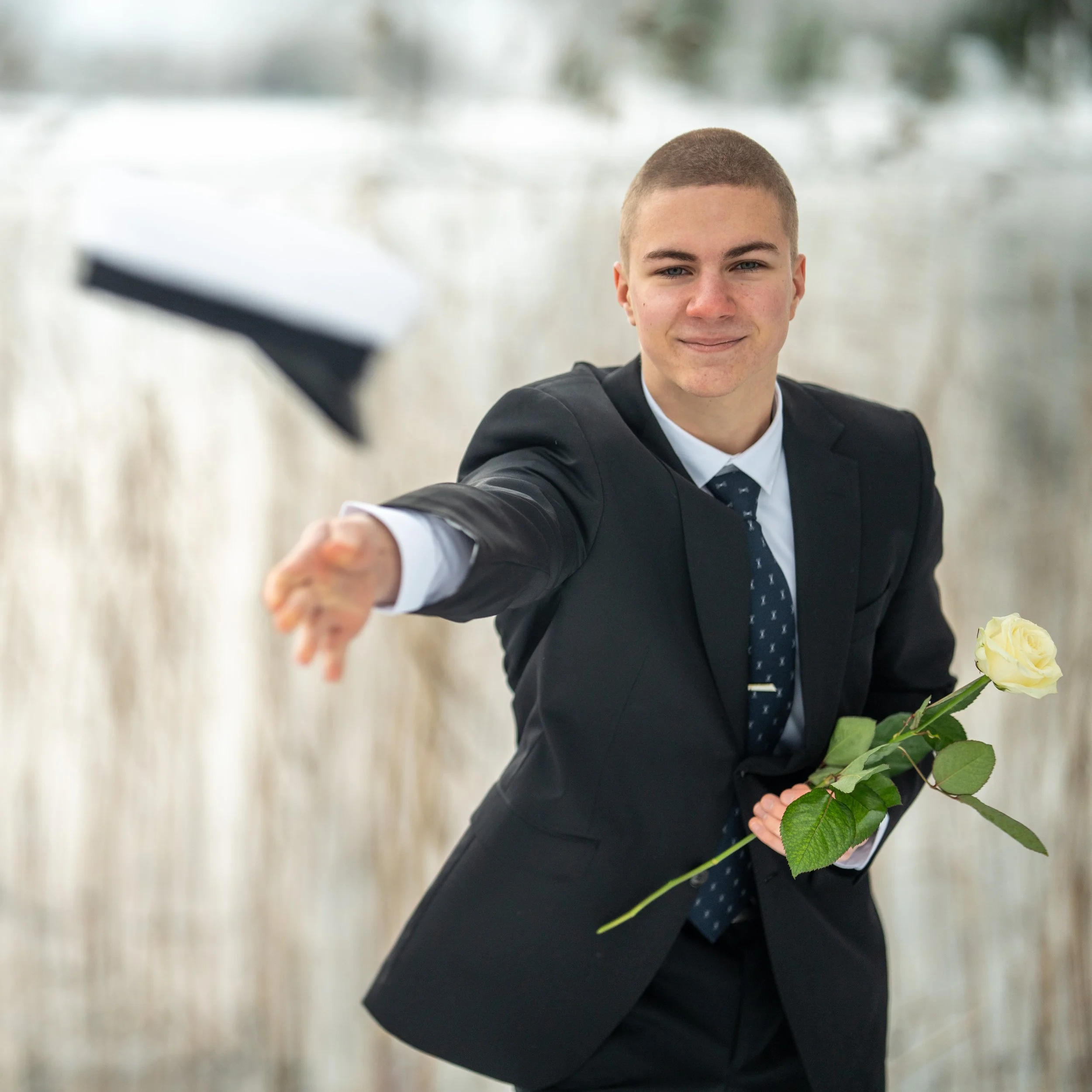 Young man in a suit holding a white rose and tossing his graduation cap in the air