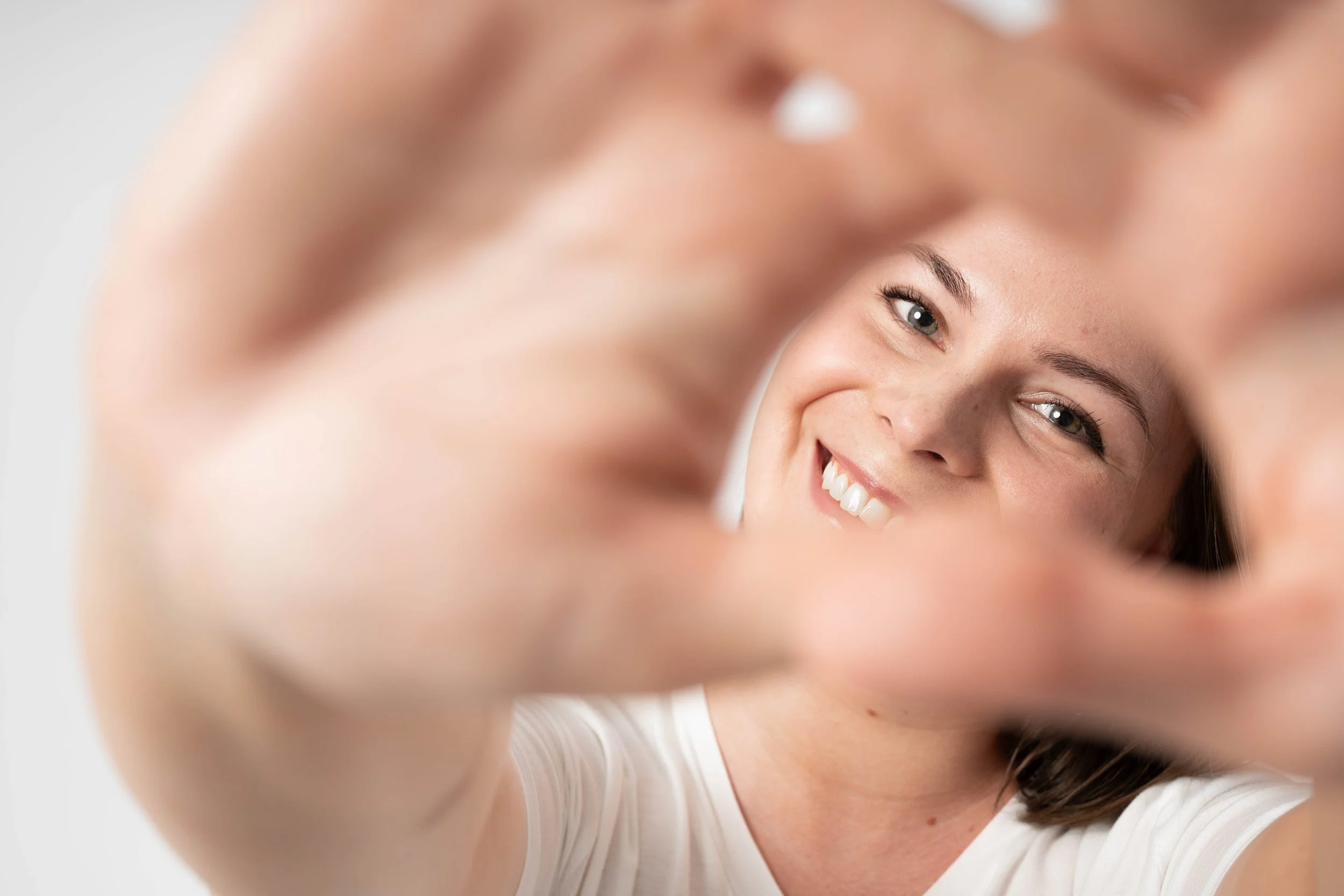 Close-up of a young woman smiling, leaning forward, with her hand forming a heart shape around her face.